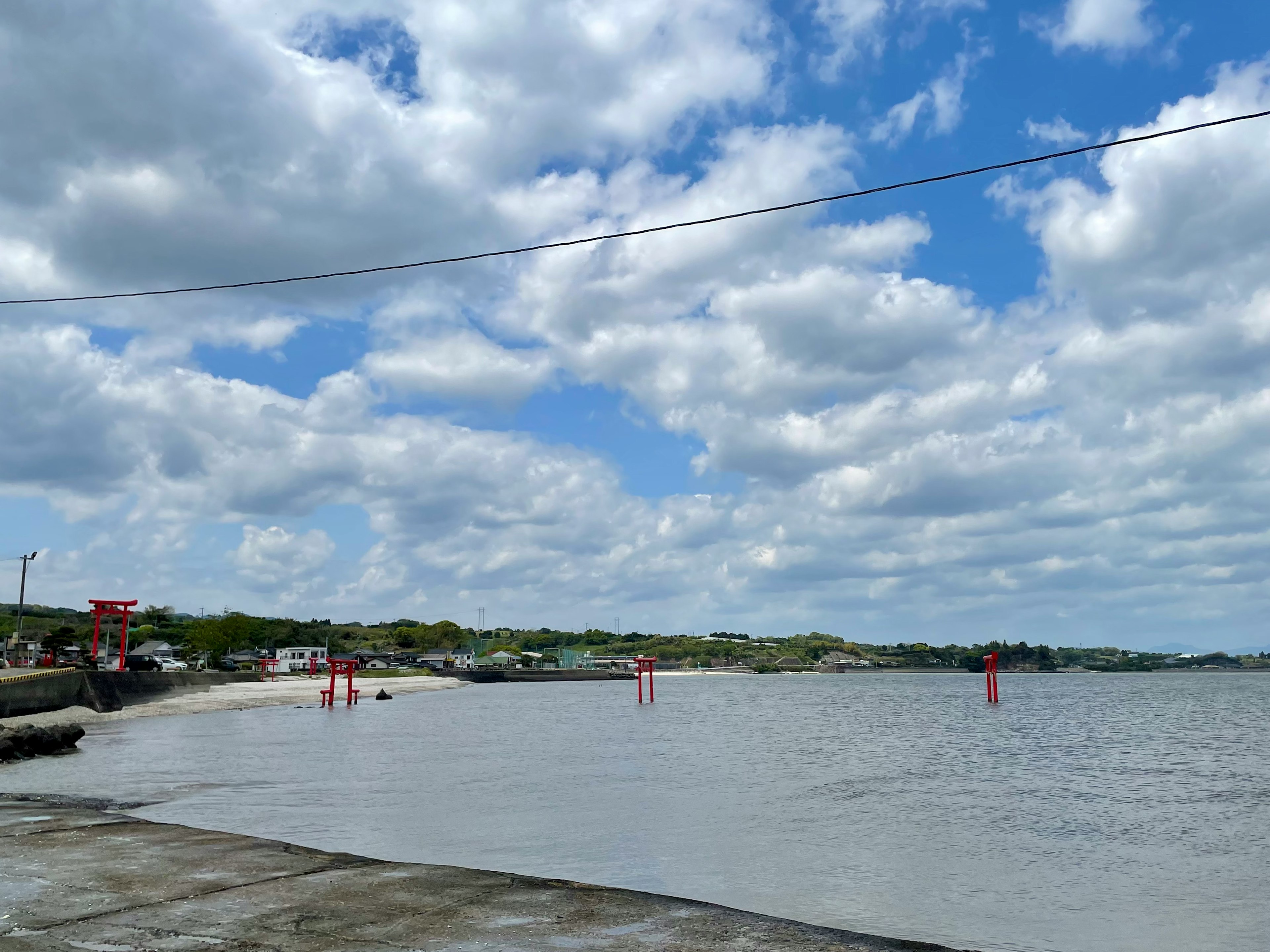 Pemandangan pantai yang tenang dengan langit biru dan awan putih berbulu penanda merah dan ombak tenang