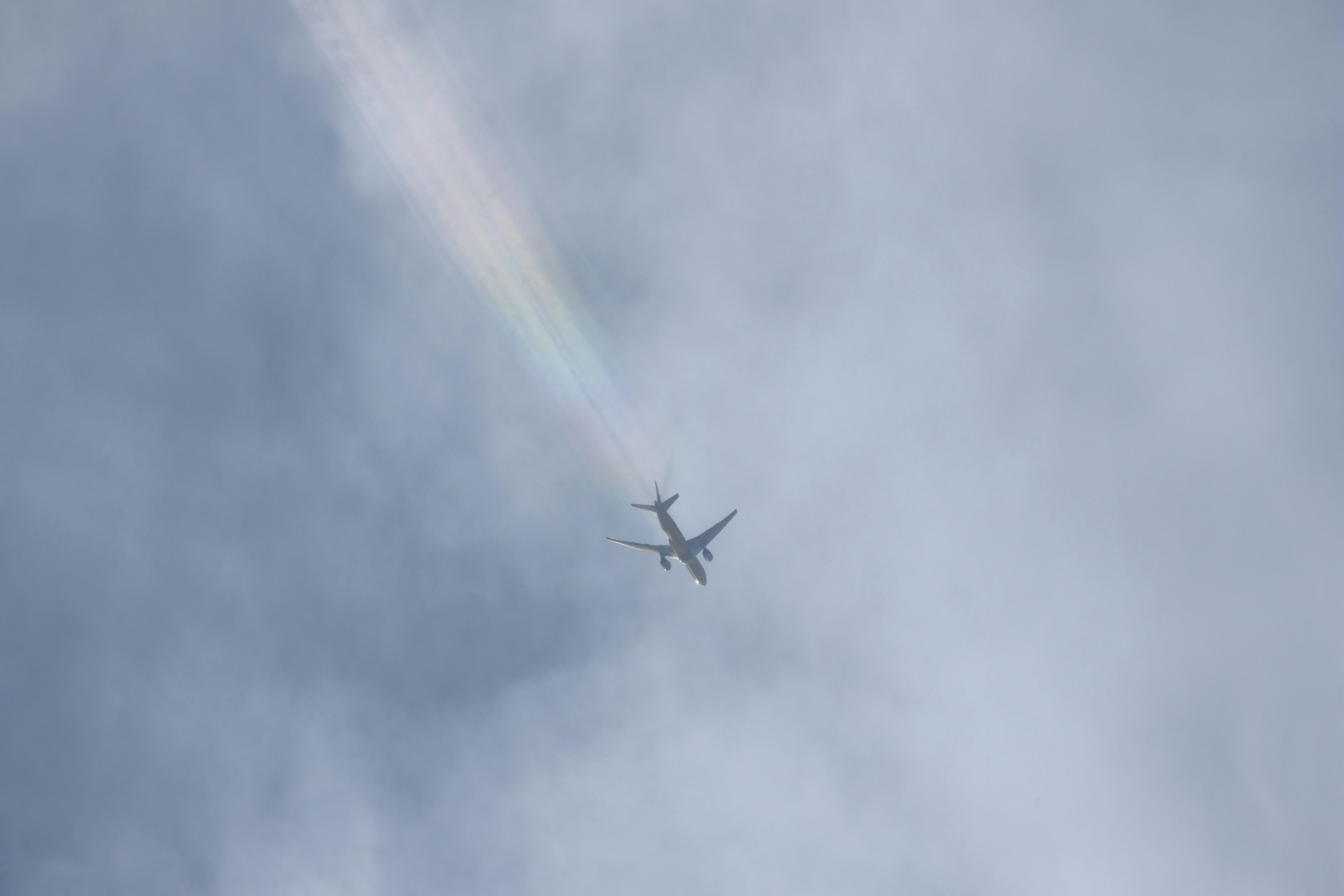 Flugzeug fliegt am Himmel mit einem Regenbogenstrahl dahinter