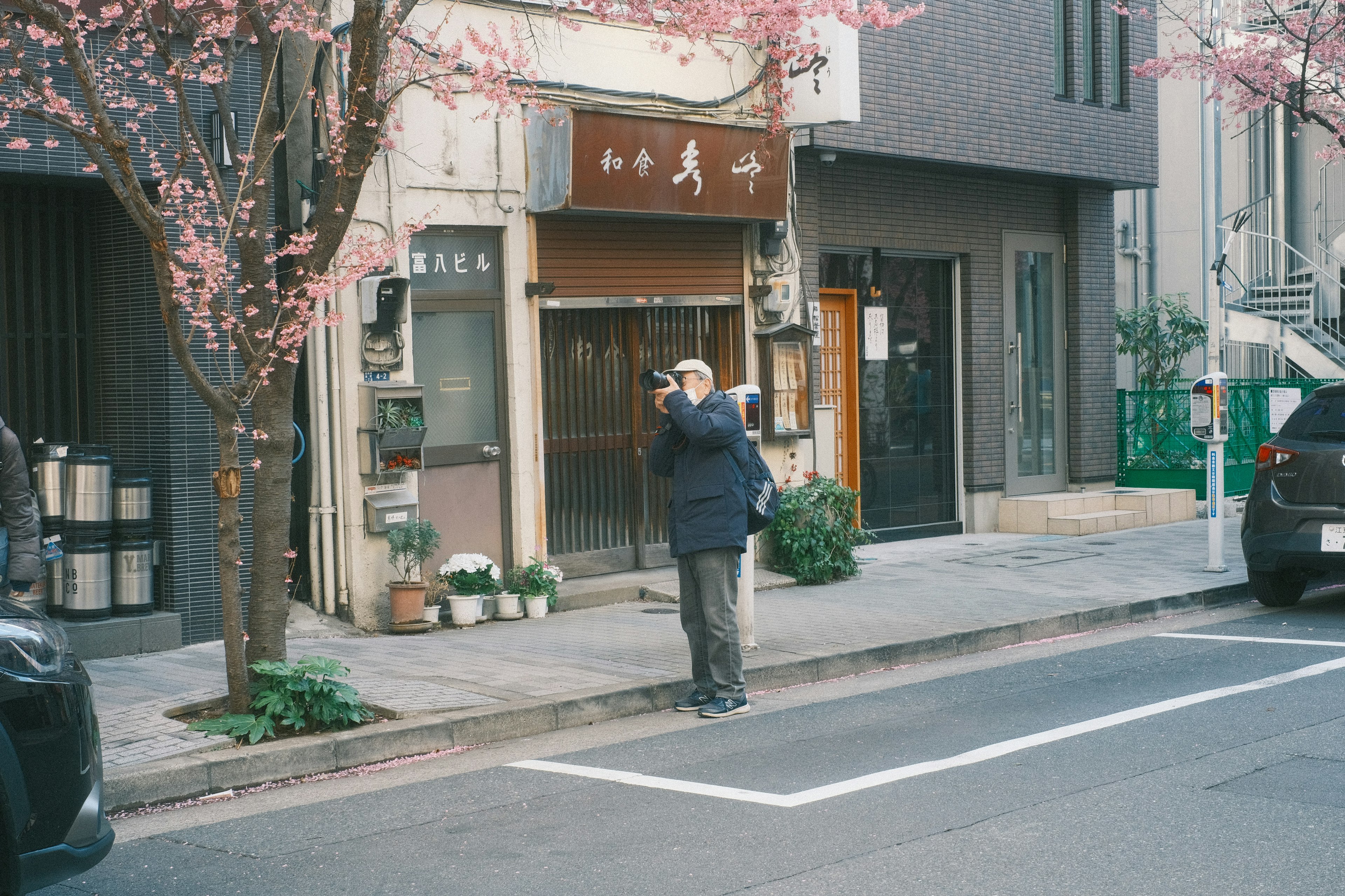 Un hombre tomando una foto frente a un árbol de cerezo y una tienda japonesa tradicional