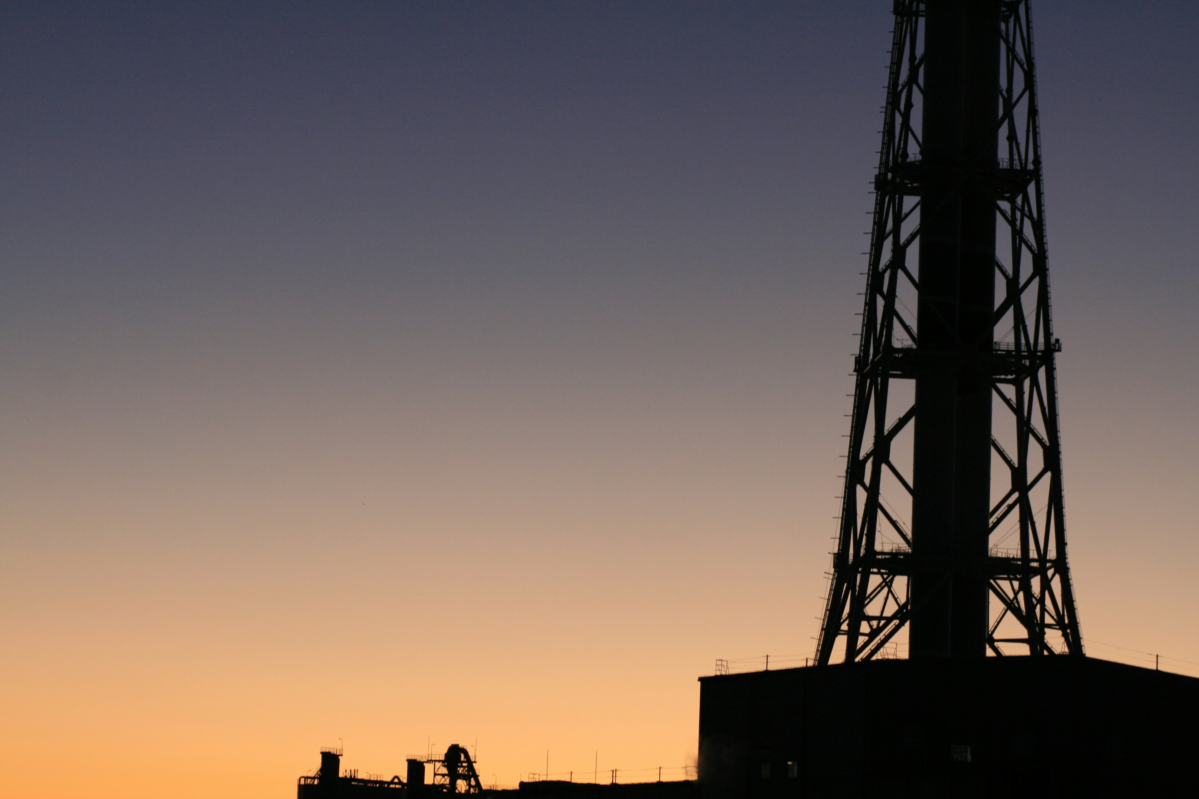 Silhouette di una torre di comunicazione e di un edificio contro un cielo al tramonto