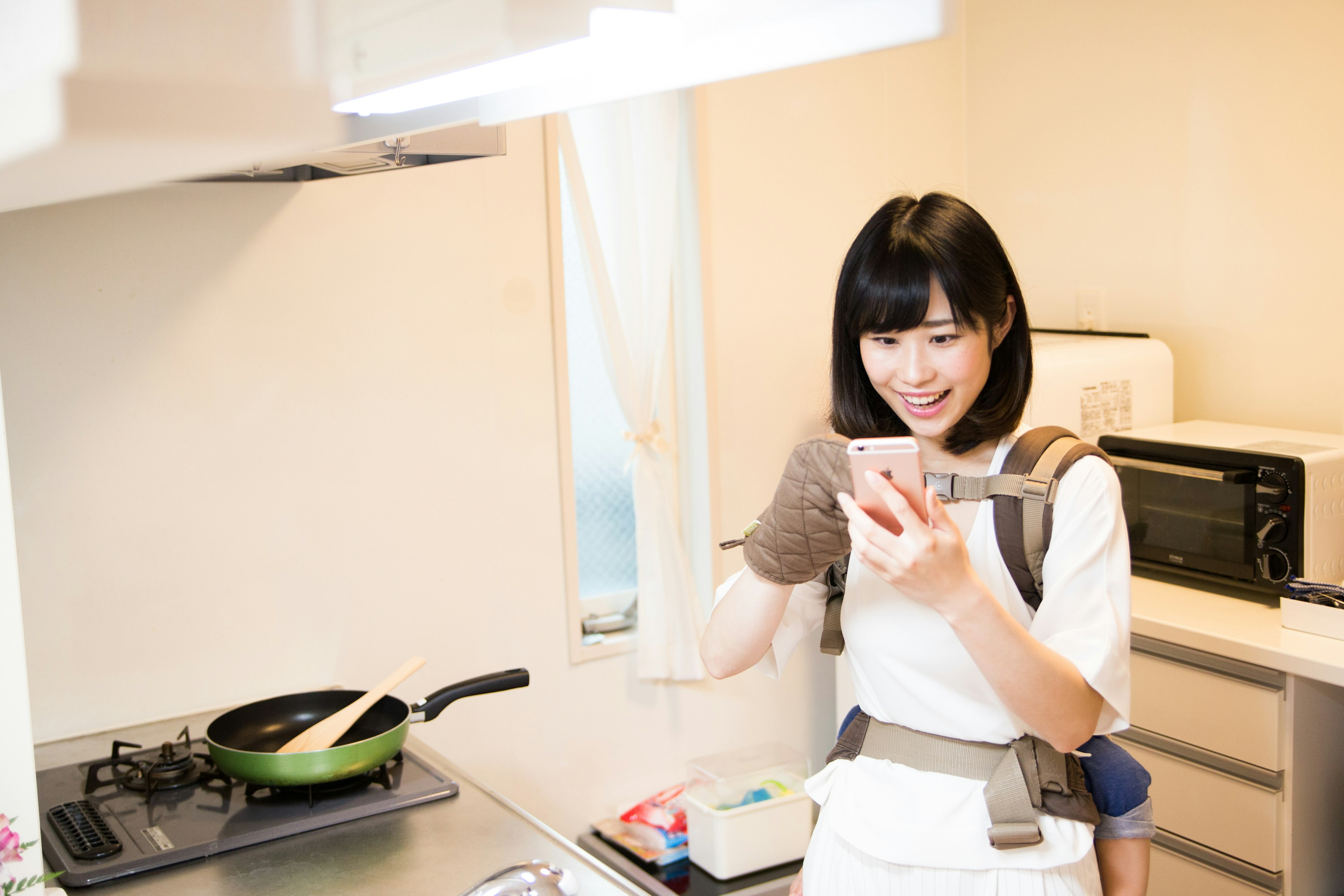 キッチンでスマートフォンを見ながら料理をする女性