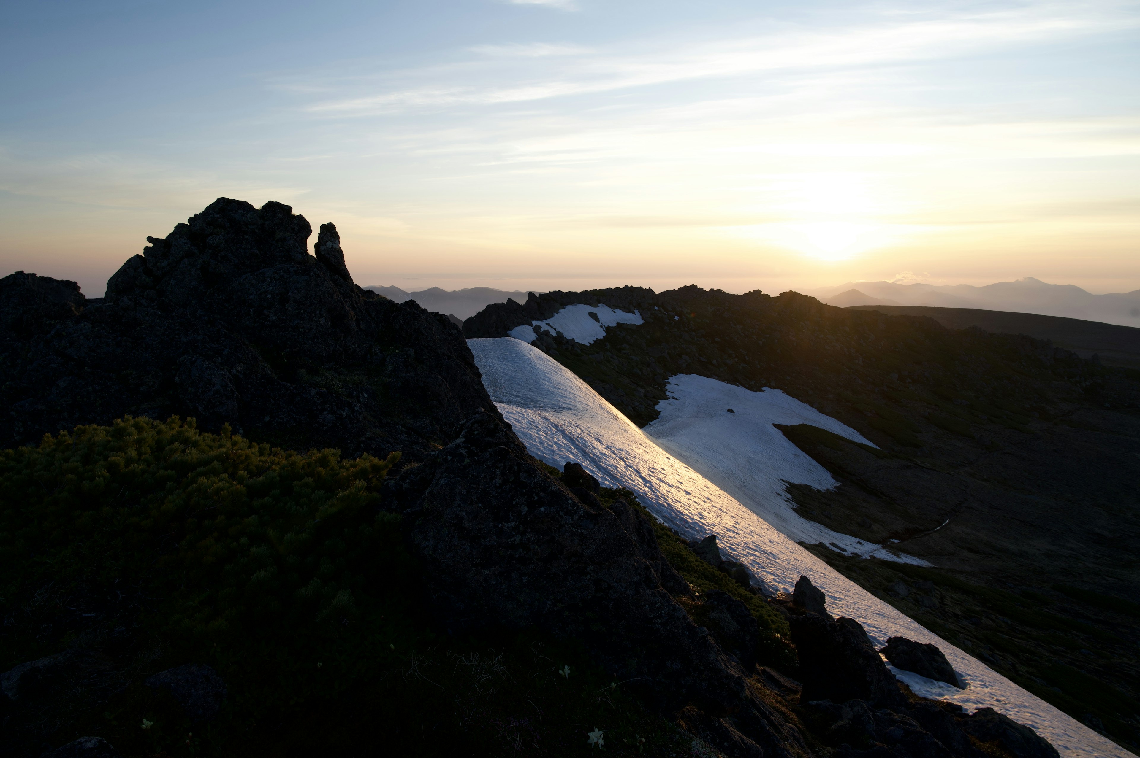 山の風景に沈む夕日と雪の残る斜面