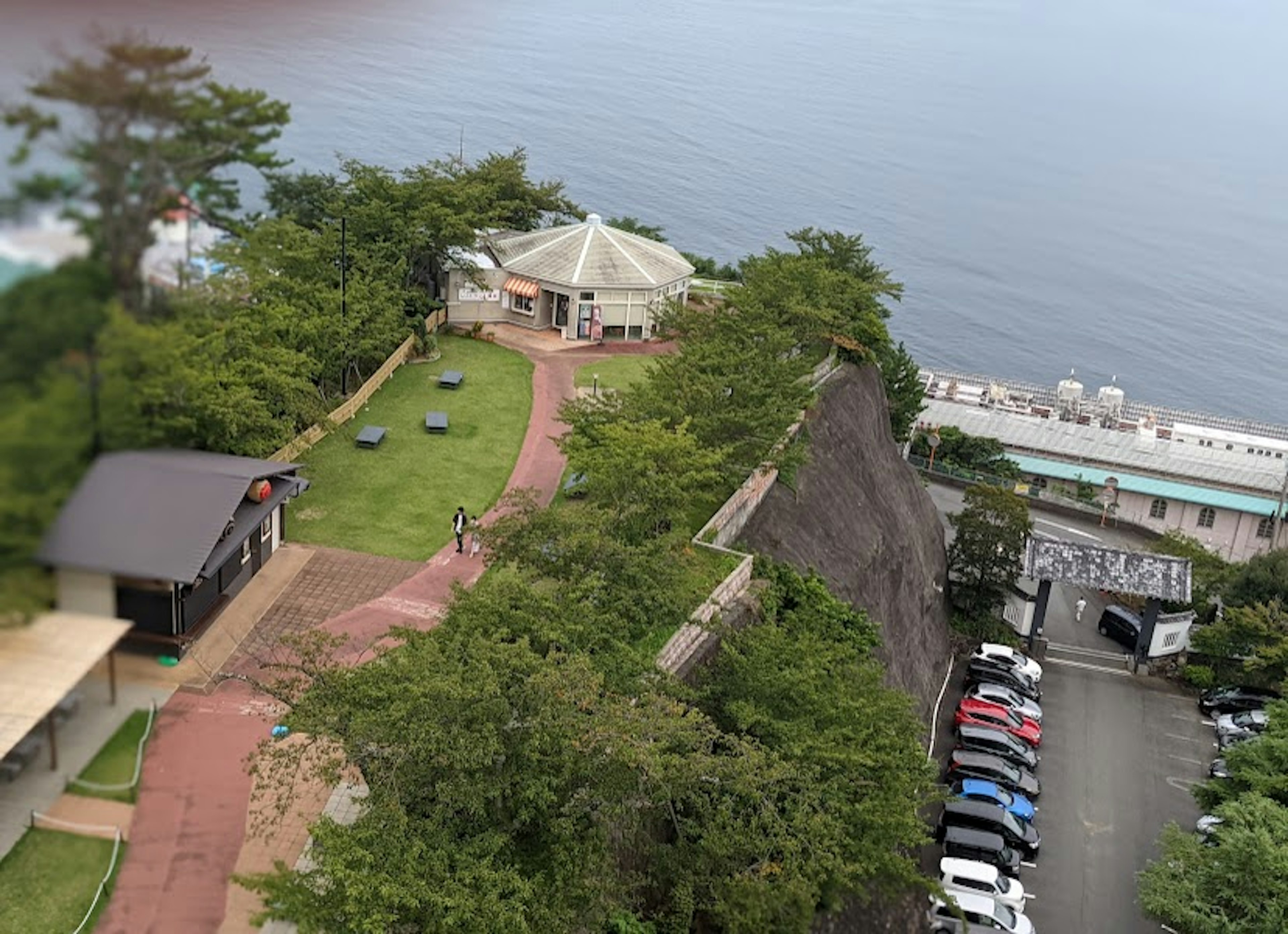 Scenic view of a green park by the sea featuring a gazebo and nearby buildings