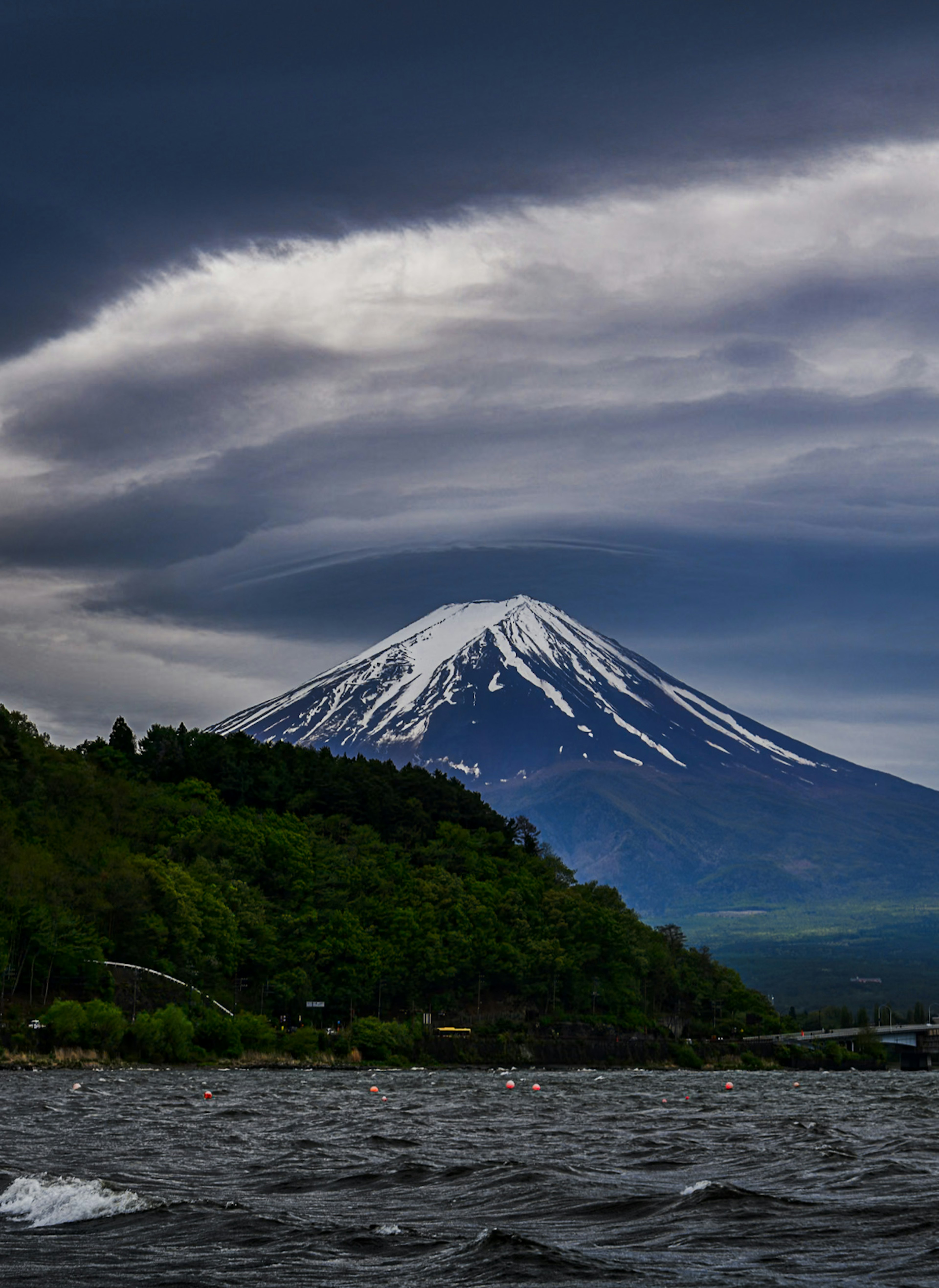 Mont Fuji avec son sommet enneigé entouré de collines verdoyantes et de nuages sombres