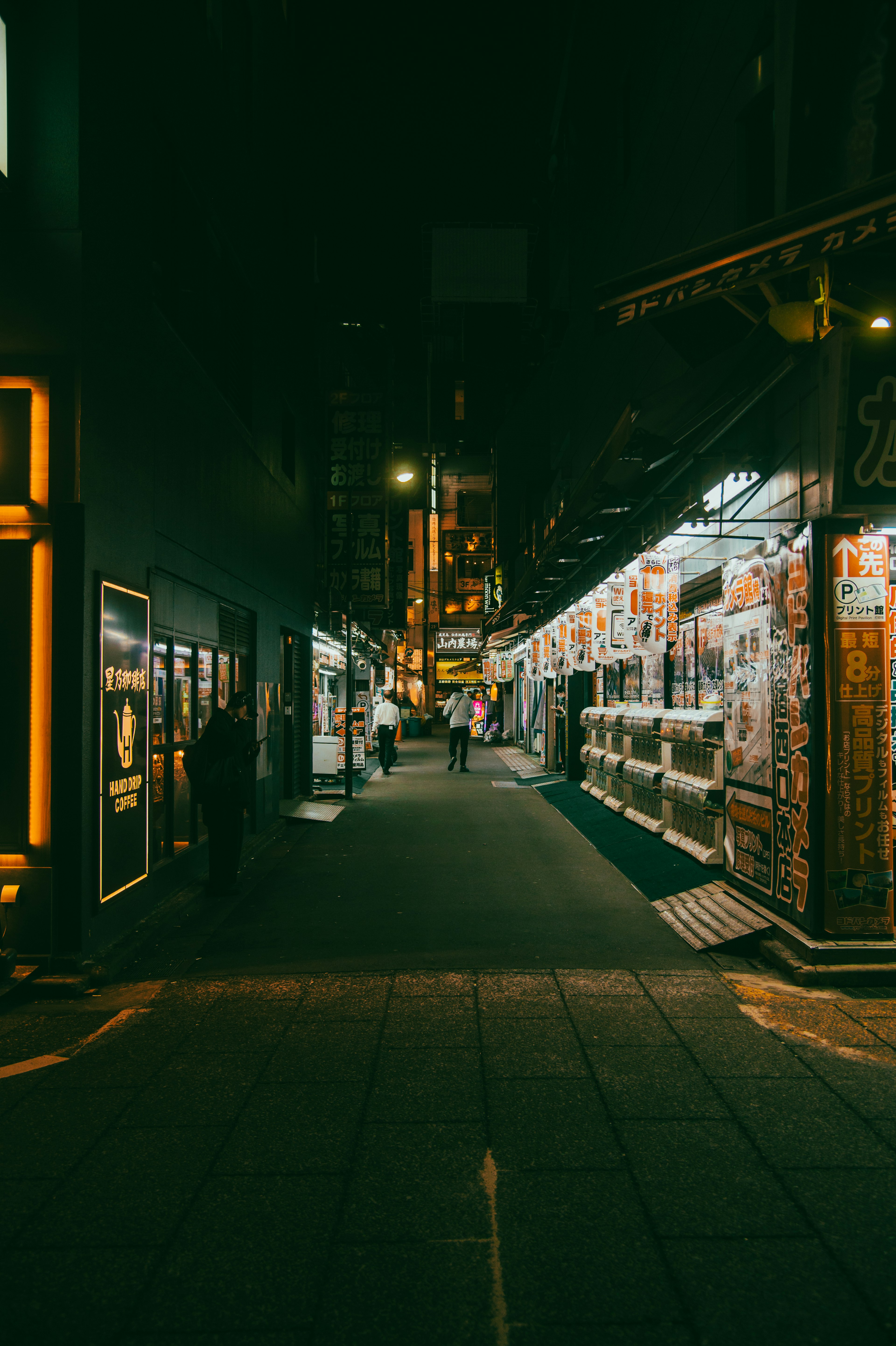 Narrow street at night with bright signs and storefronts