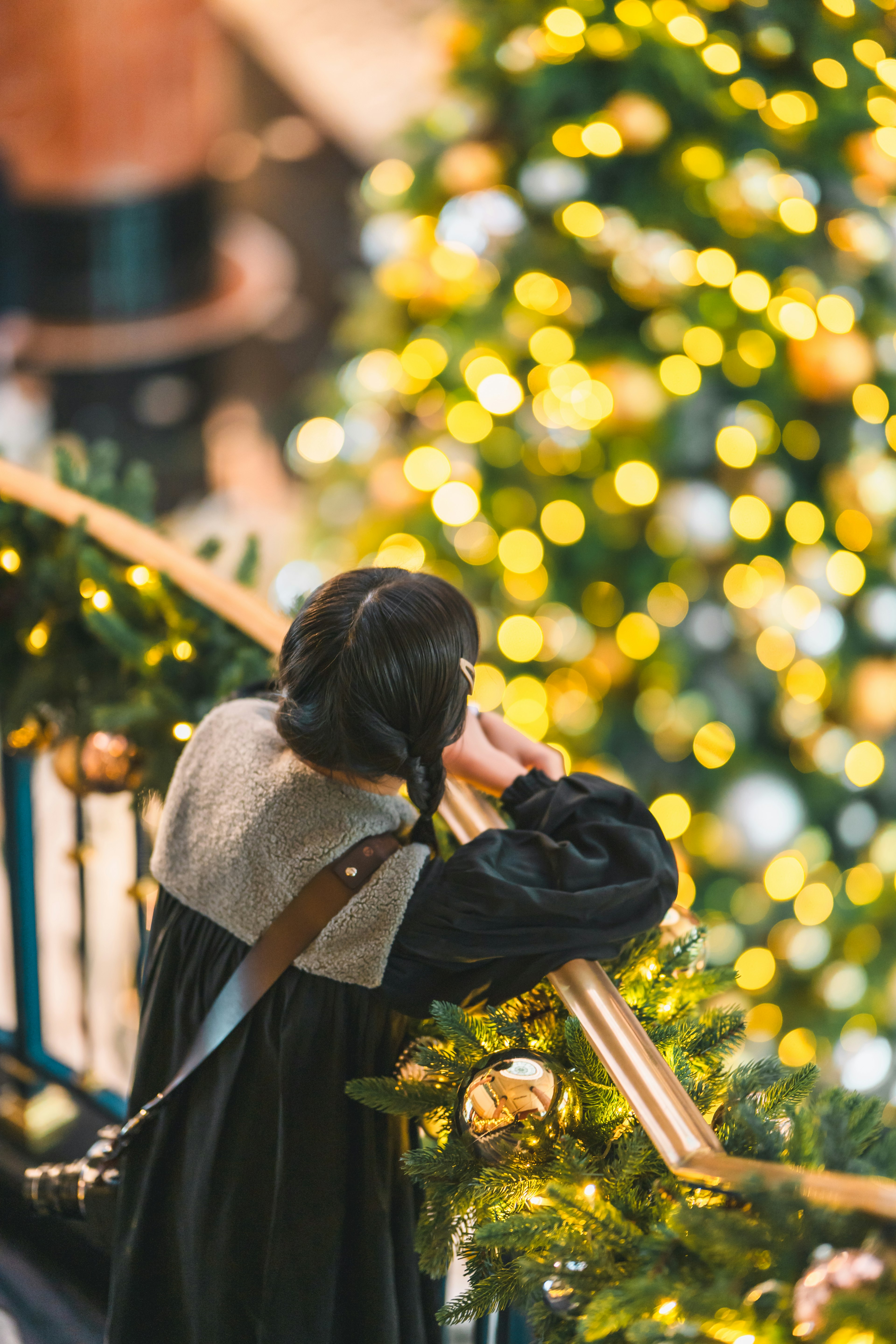 Una mujer con un vestido negro y una capa clara está junto a un árbol de Navidad decorado