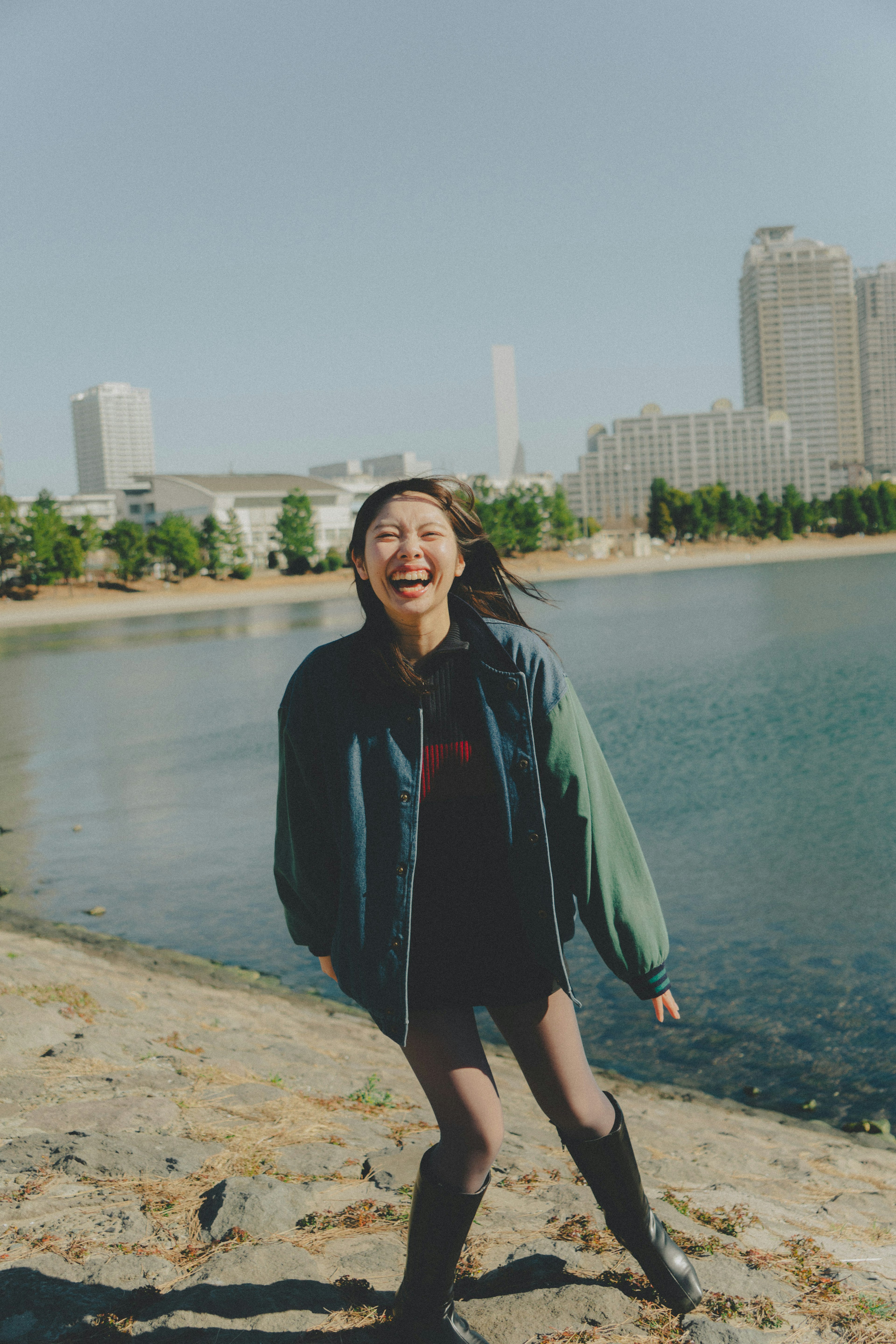 A smiling woman standing by the water with skyscrapers in the background