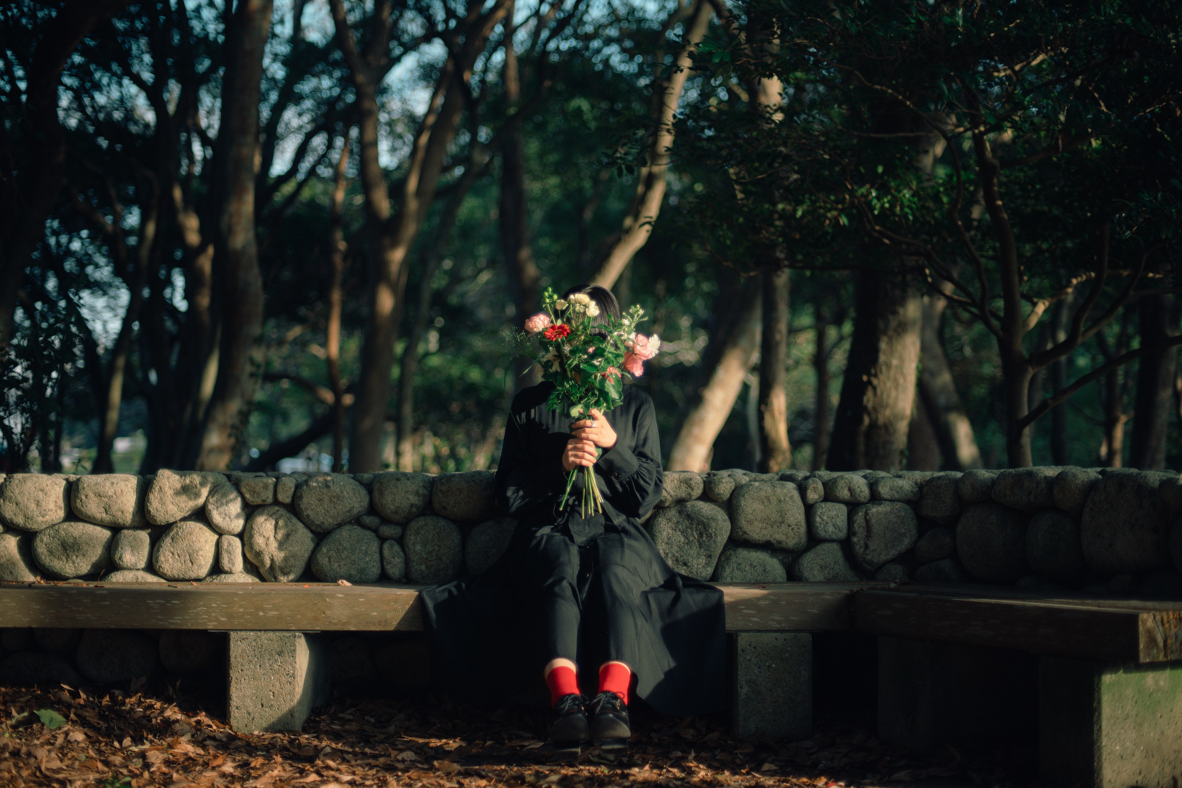 公園のベンチに座る黒い服の人物が花束を持っている