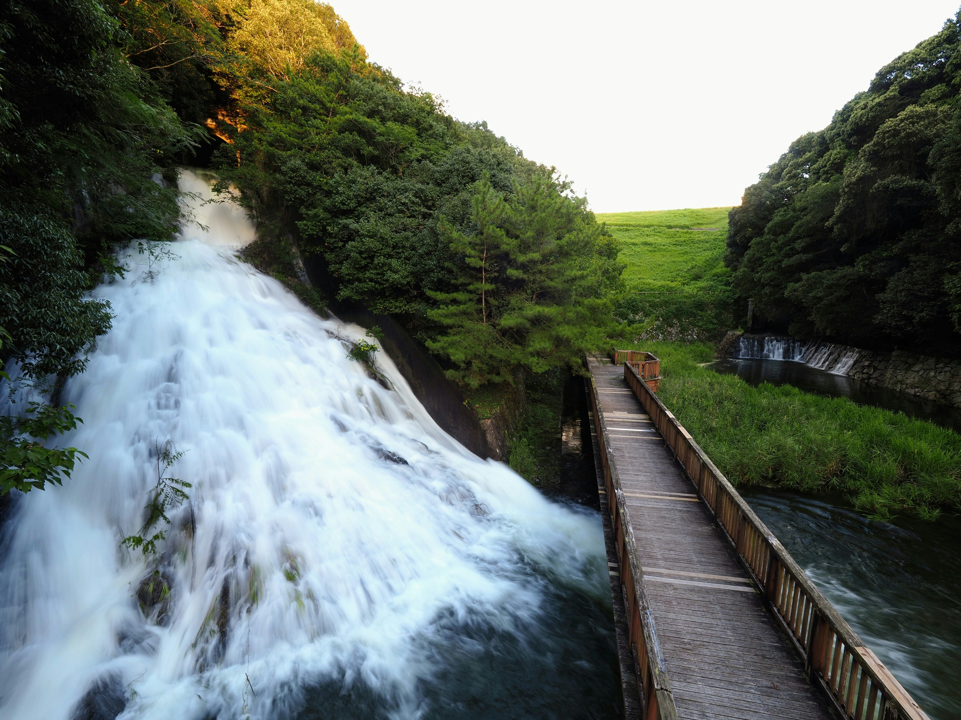 Malersicher Blick auf einen Wasserfall umgeben von Grün mit einem Holzweg