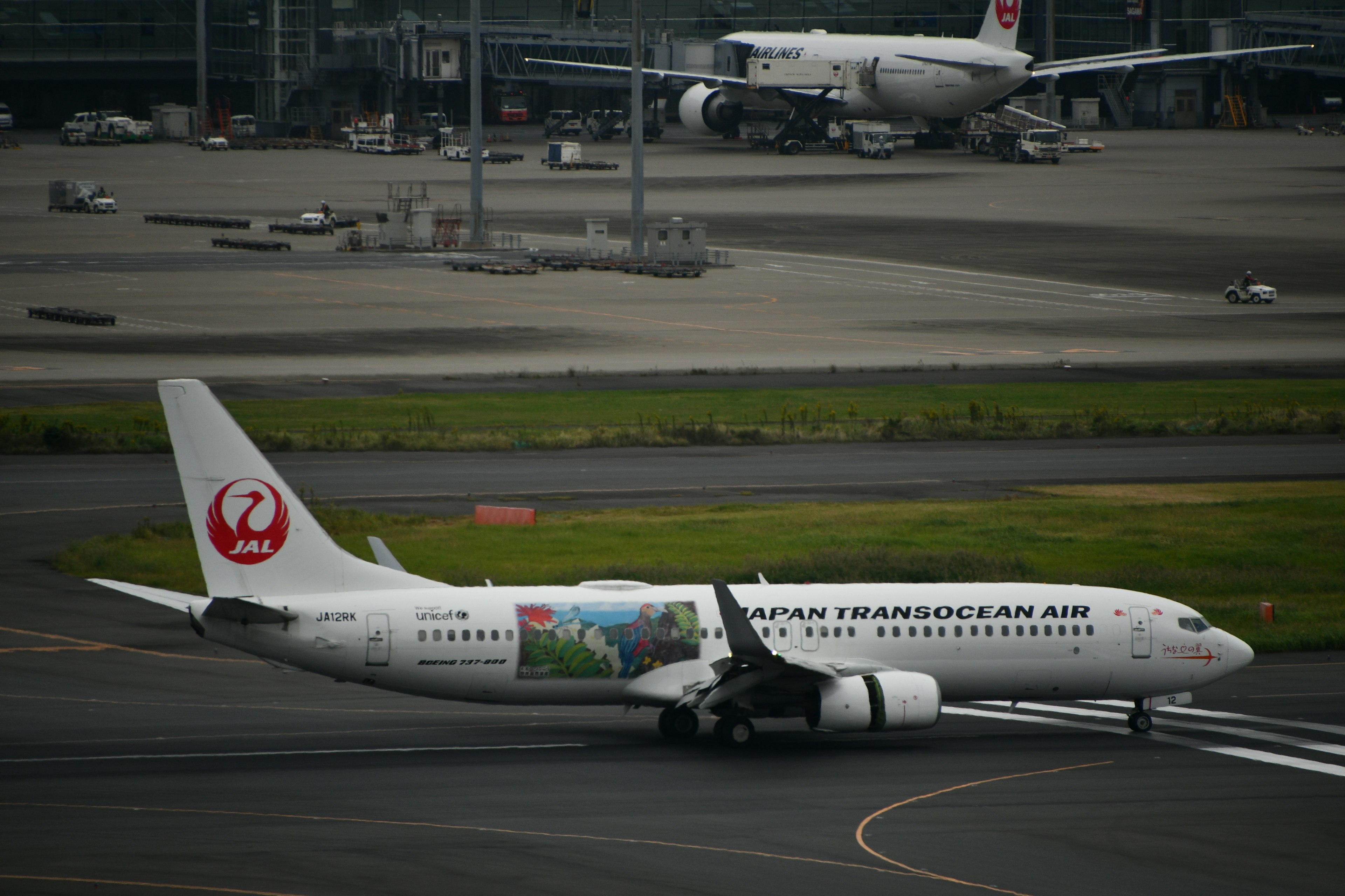 Japan Airlines Flugzeug, das auf der Startbahn rollt, mit einem anderen Flugzeug im Hintergrund