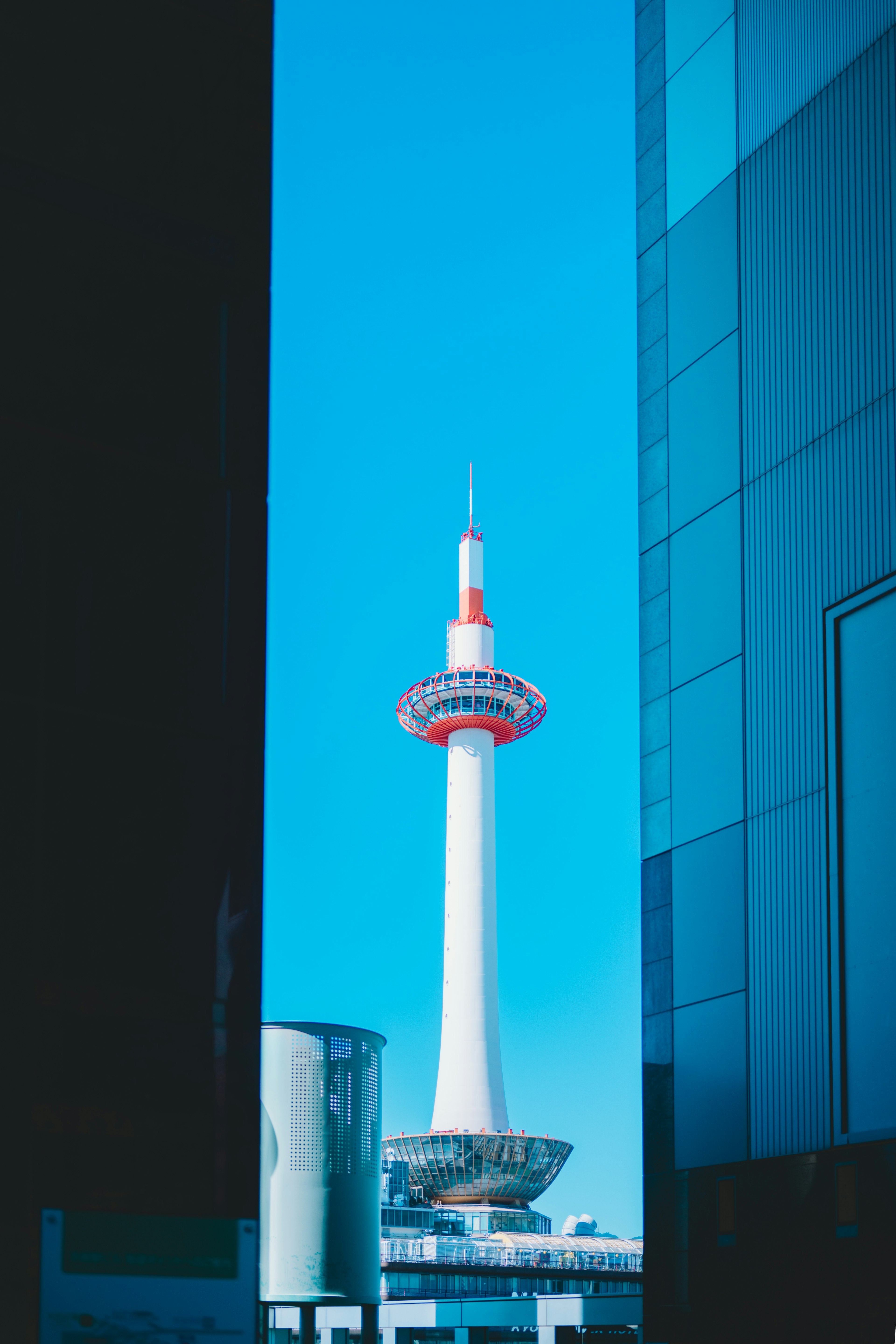 View of Kyoto Tower framed between modern buildings under a clear blue sky