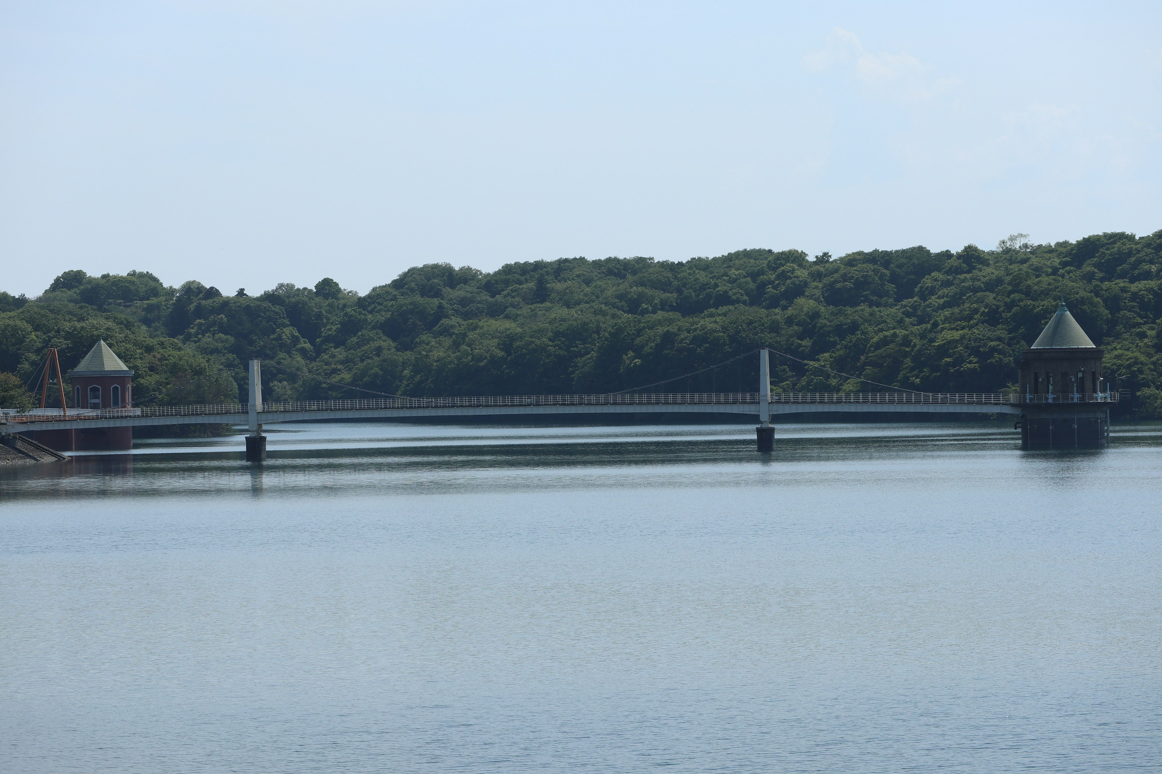 A bridge spanning a calm water surface surrounded by greenery with towers on either side