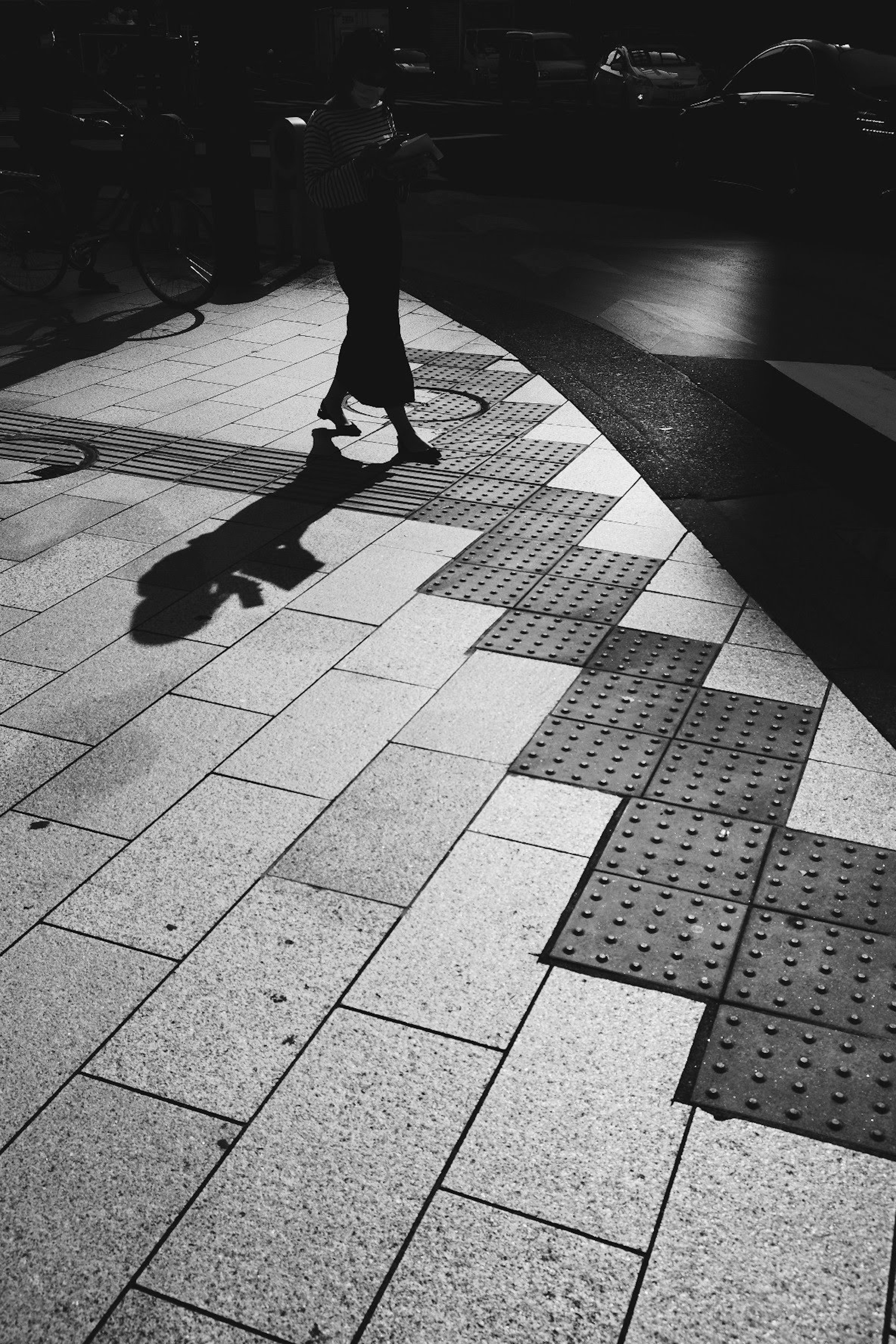 Black and white image of a person walking on a patterned pavement with shadows