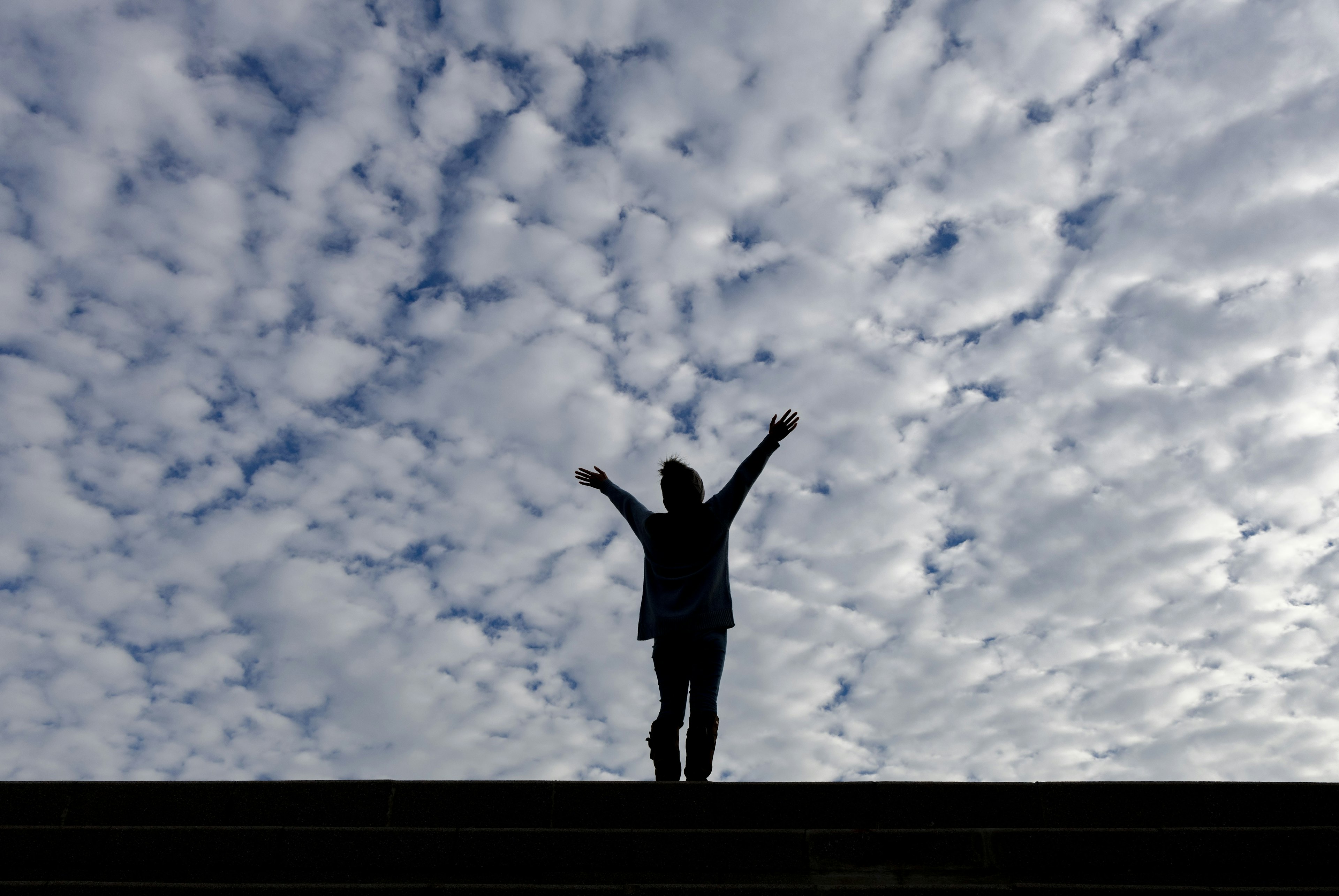 Silhouette of a person with arms raised against a backdrop of a cloudy sky