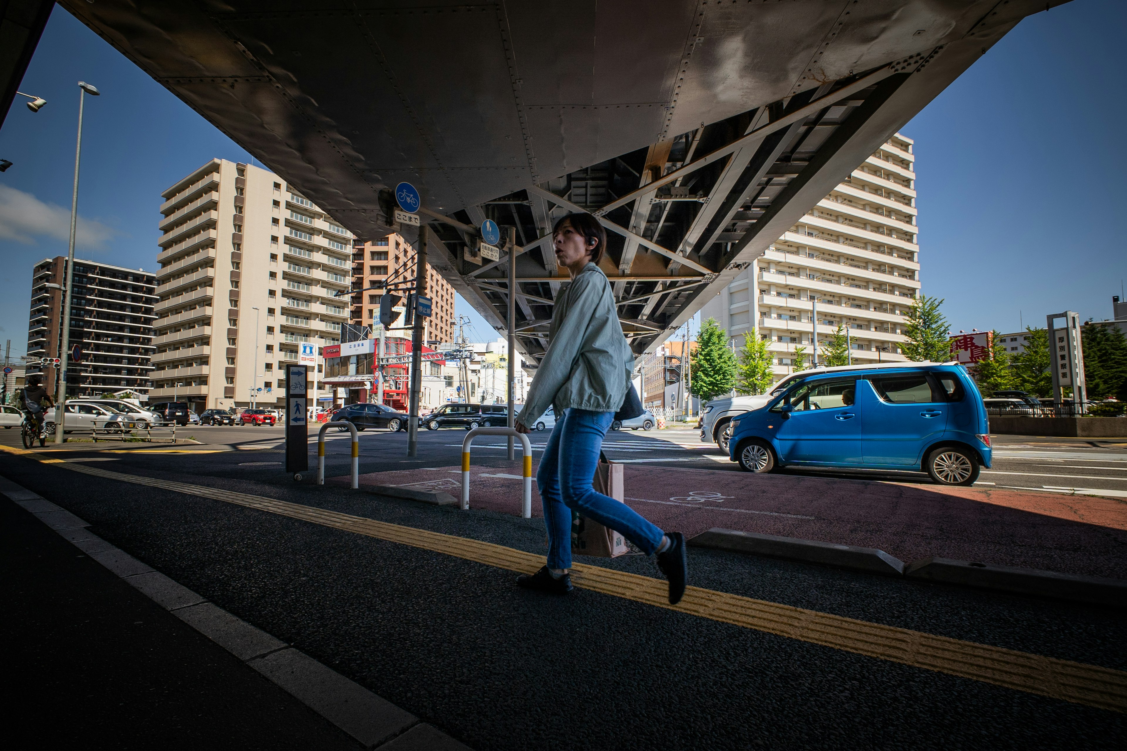 Une personne marchant dans une scène urbaine avec des bâtiments de grande hauteur et une voiture bleue