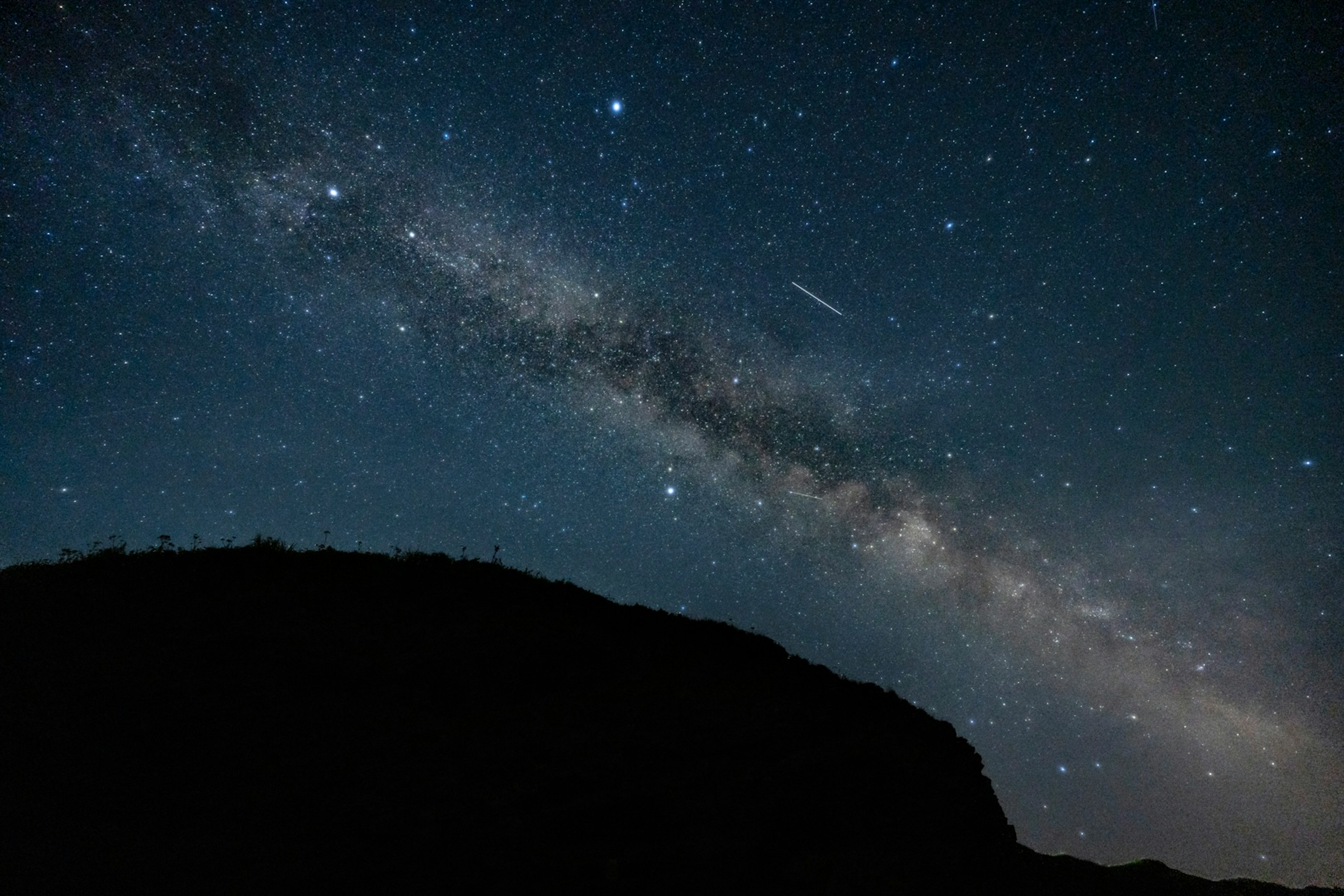 星空の中に広がる天の川と流れ星のシルエット