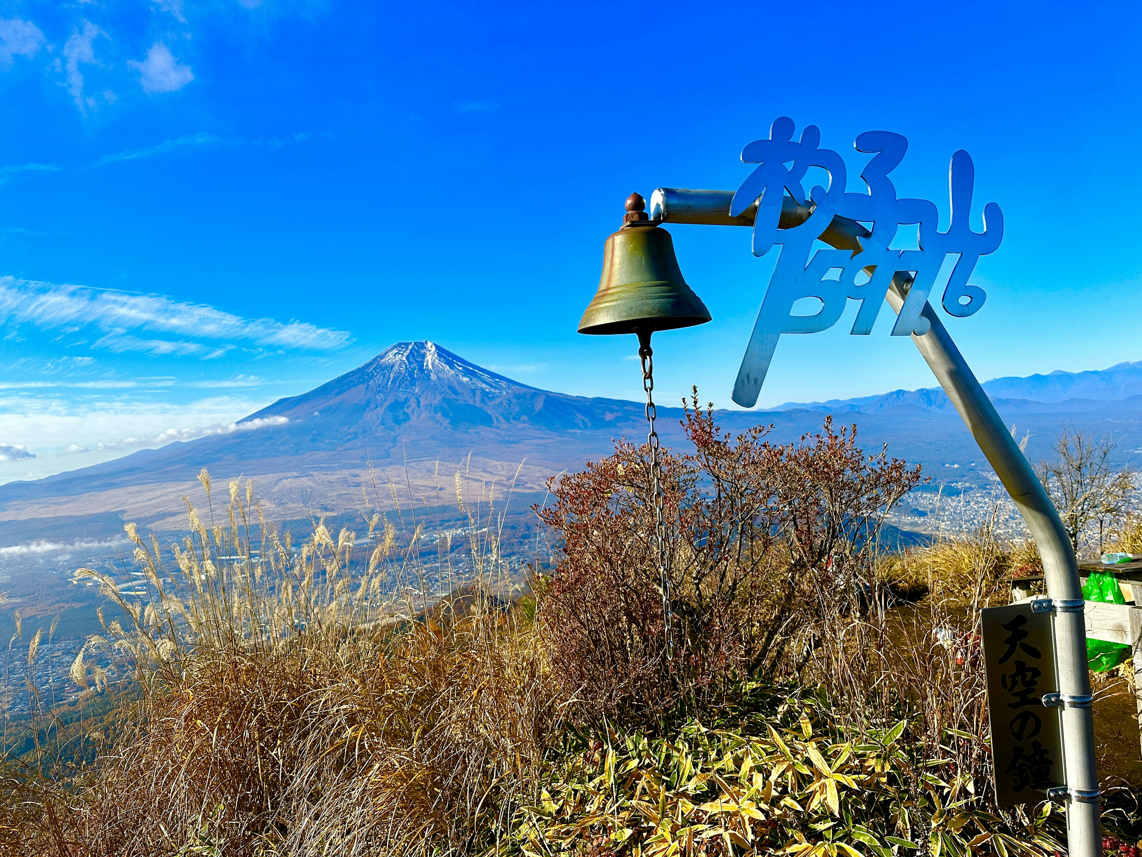 Sebuah lonceng dengan tulisan biru di latar belakang pegunungan