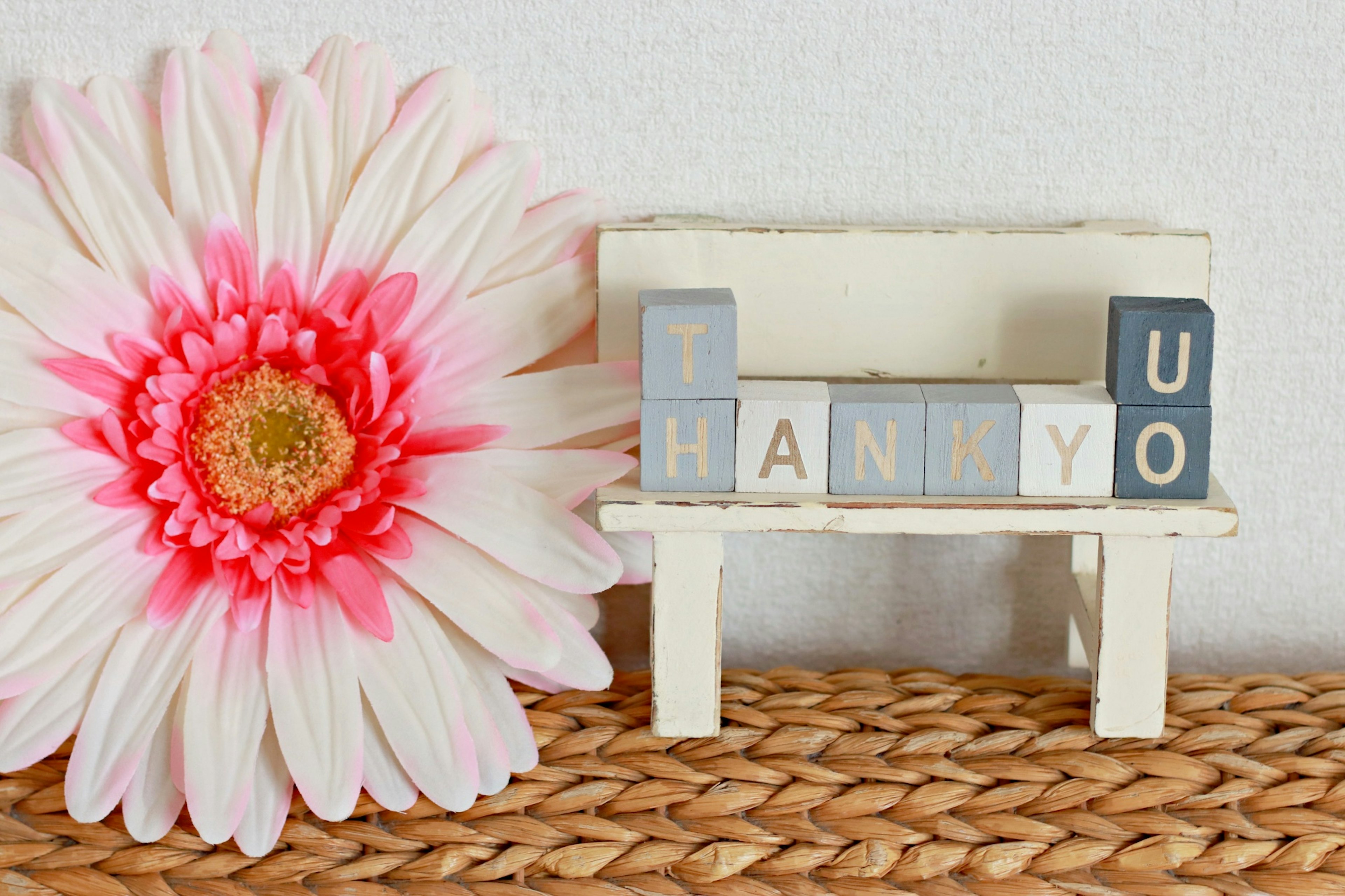 Un petit banc blanc avec des blocs de lettres écrivant merci à côté d'une grande fleur rose