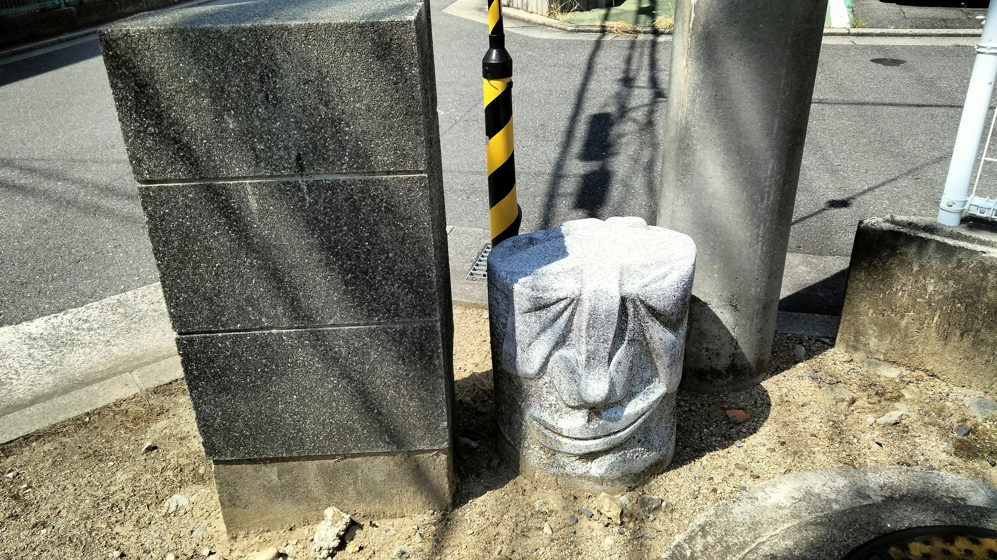 Two stone pillars beside the road with a concrete block shaped like a face