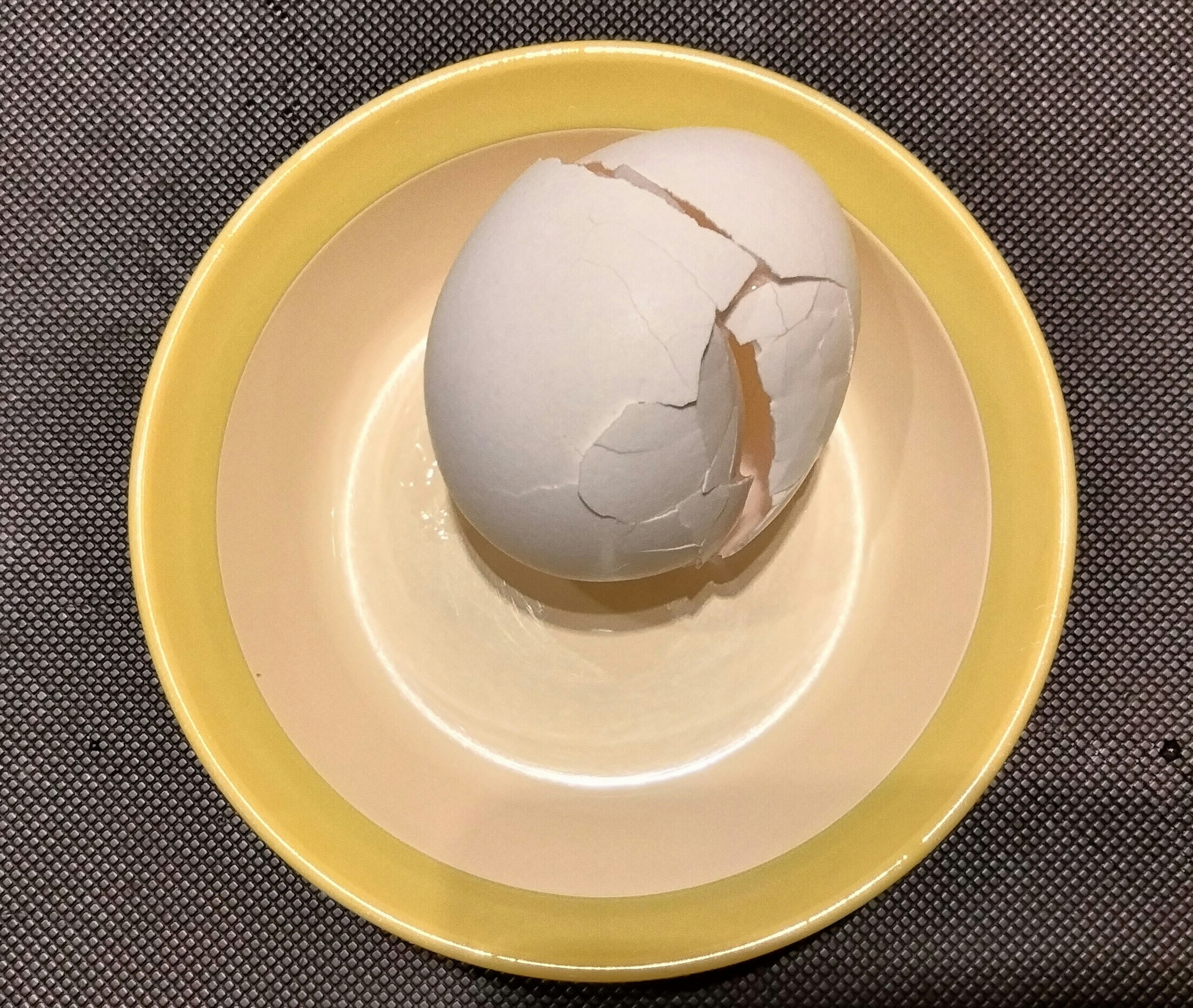 A cracked white egg resting in a yellow bowl