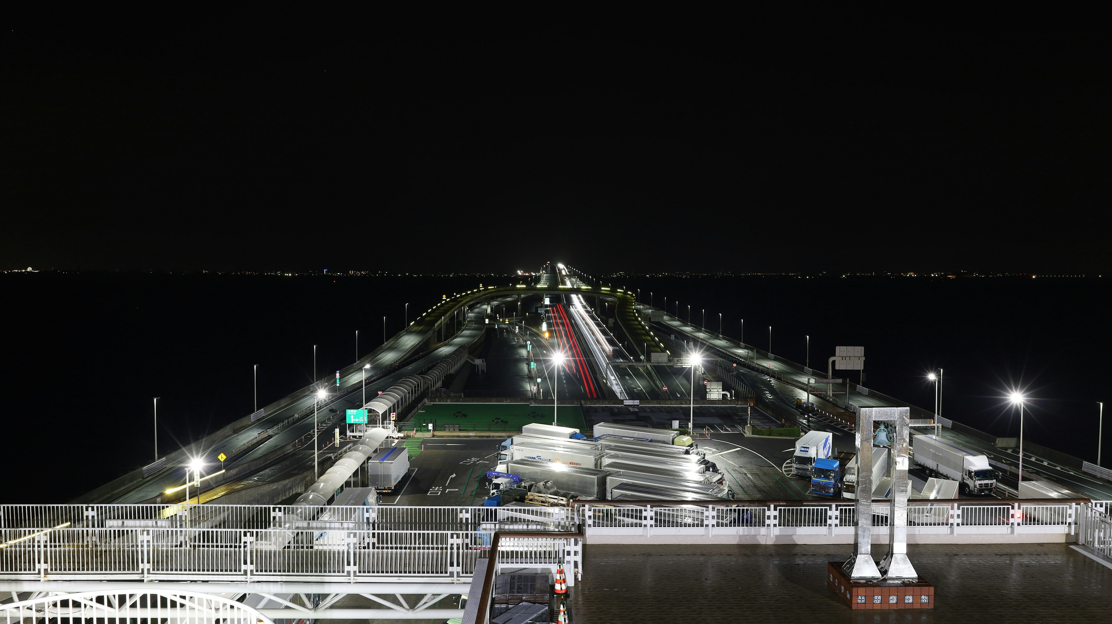 Pemandangan jembatan yang membentang ke laut malam dengan lampu mobil yang bersinar