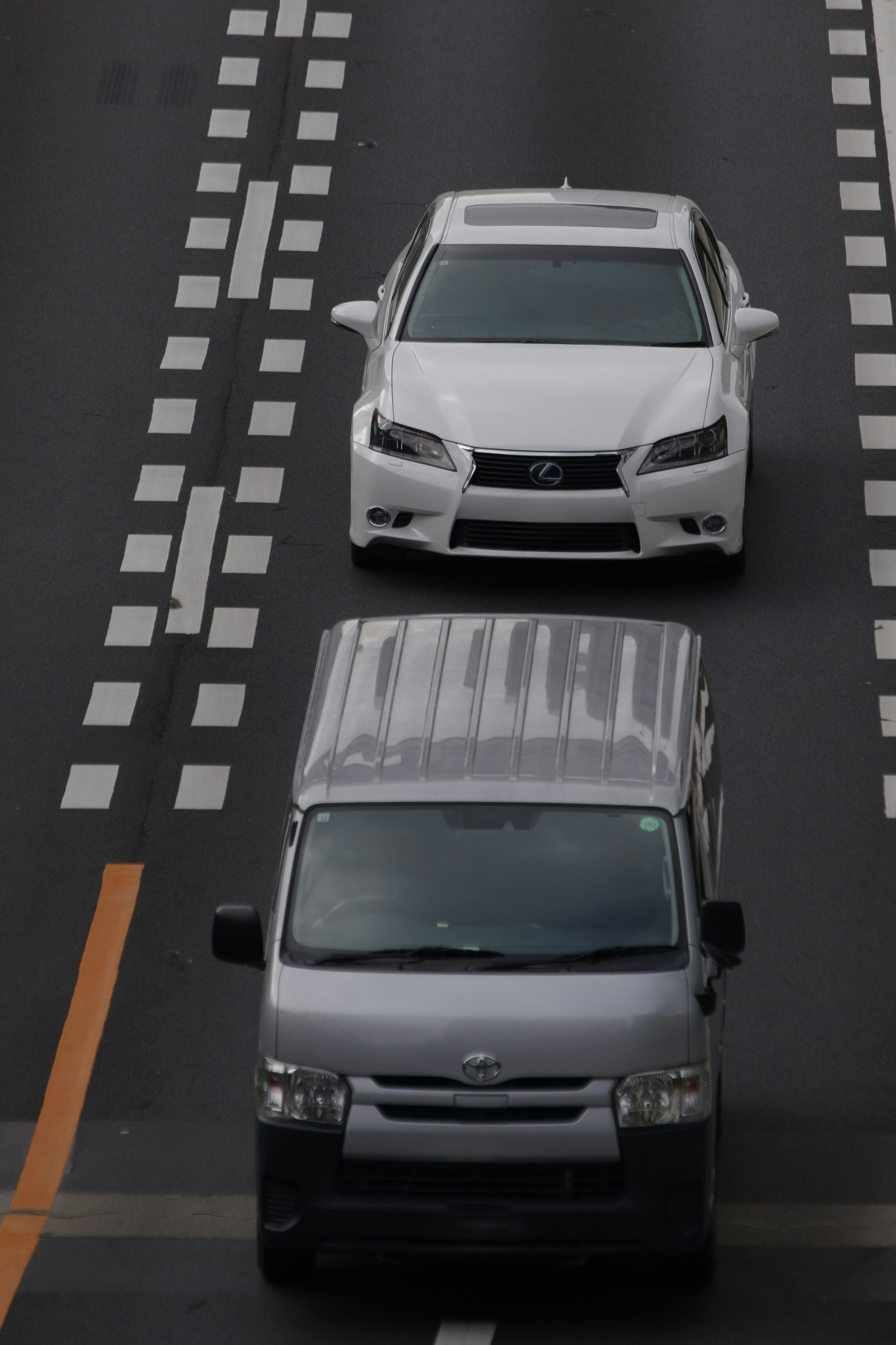 A white car and a gray van driving on a road