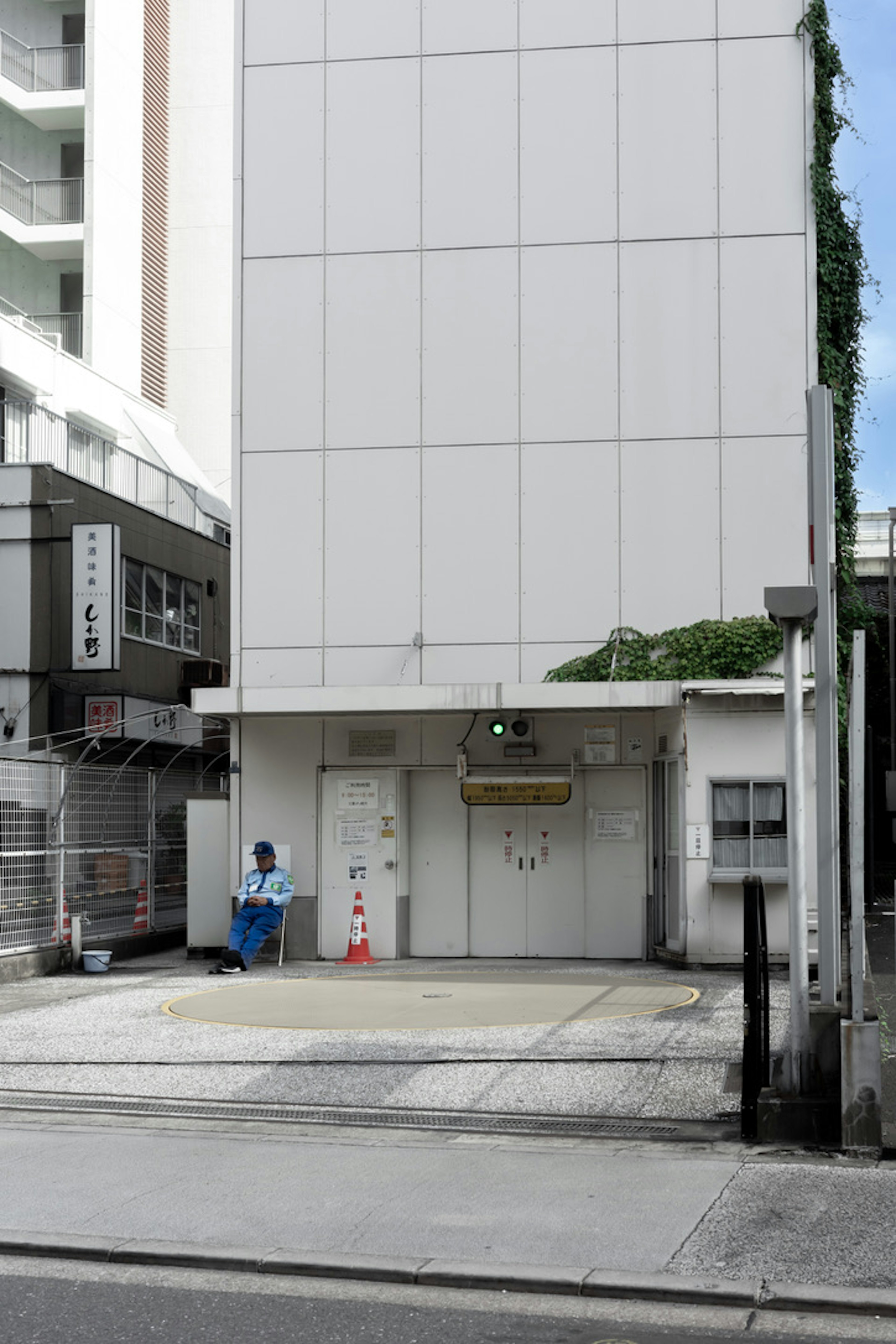 青い服を着た人物が建物の前に立っているシンプルな都市の風景