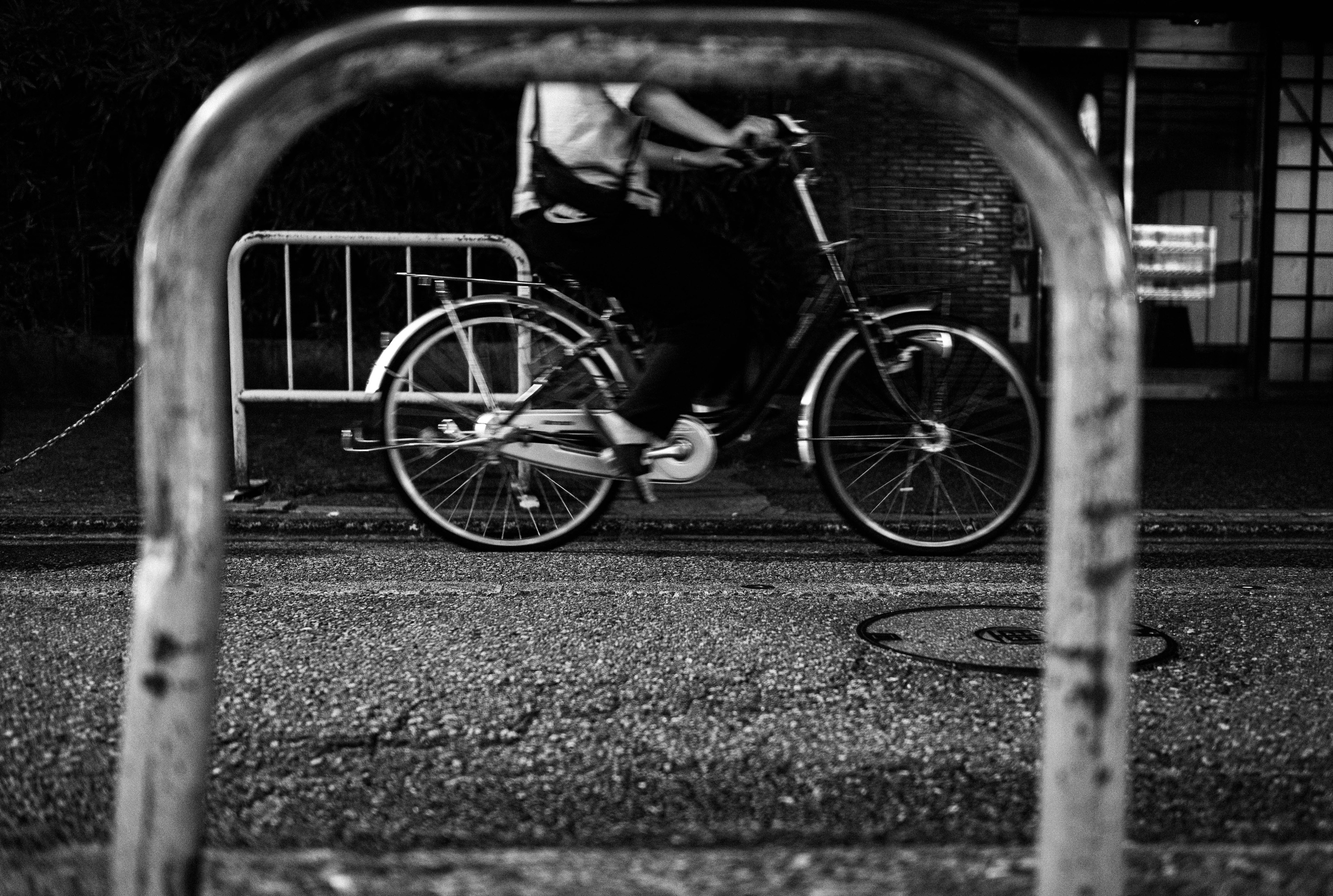 A monochrome photo of a person riding a bicycle passing through a metal barrier