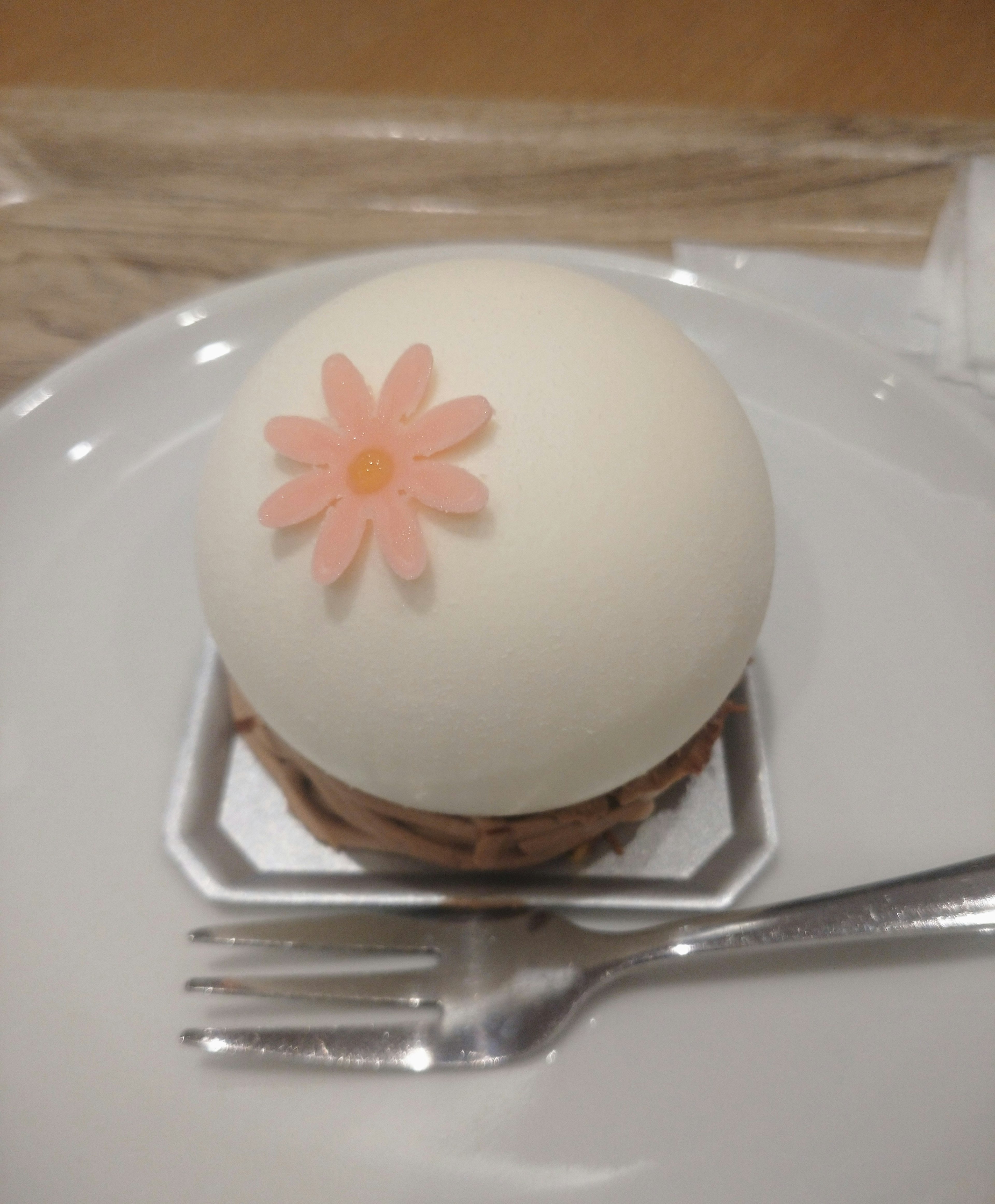 A round white cake topped with a pink flower