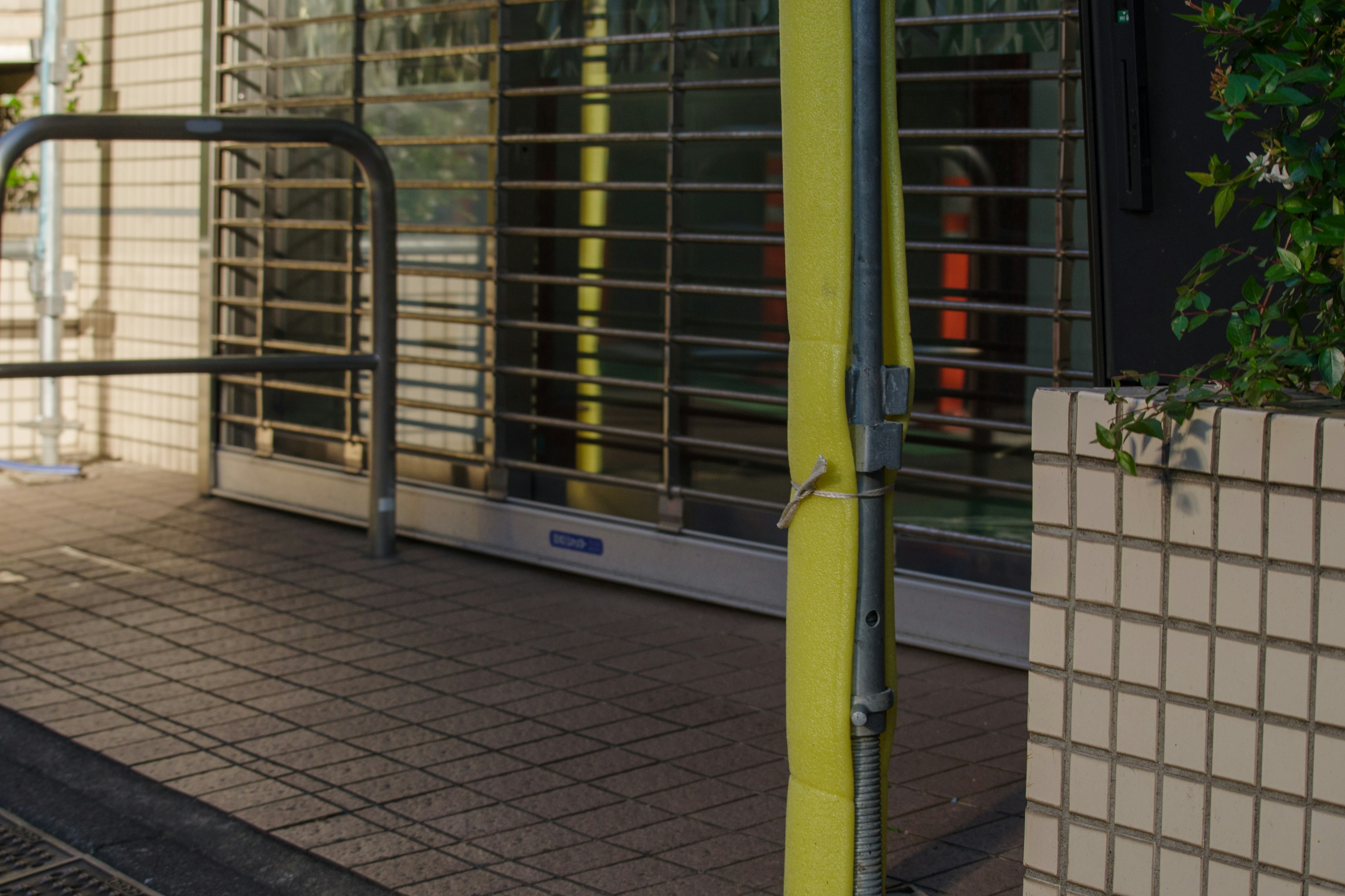 Entrada de tienda con barandilla amarilla y persiana enrejada