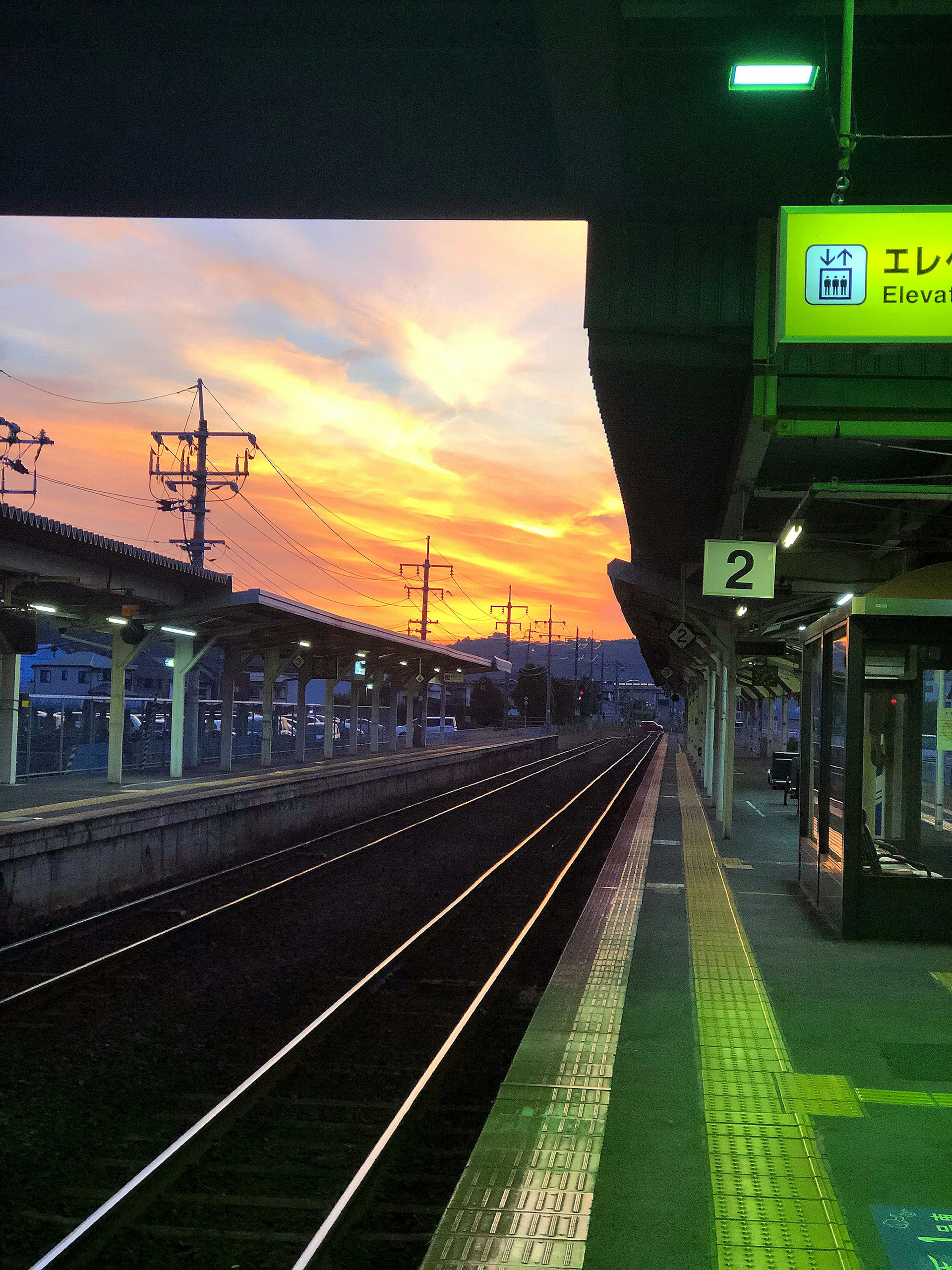 Train station platform at sunset with visible tracks and signage