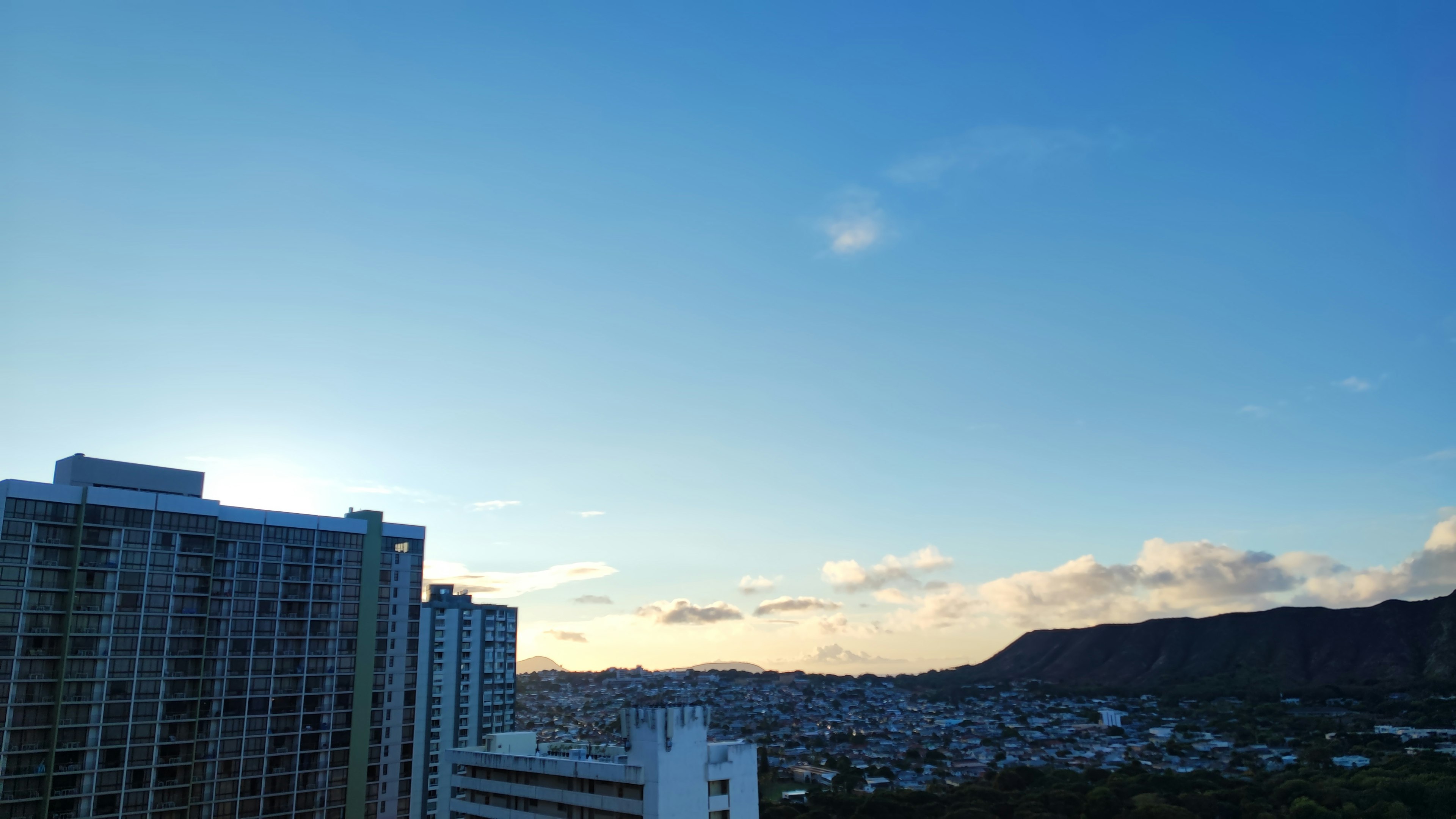 Cielo azul con nubes que muestra edificios altos y paisaje montañoso