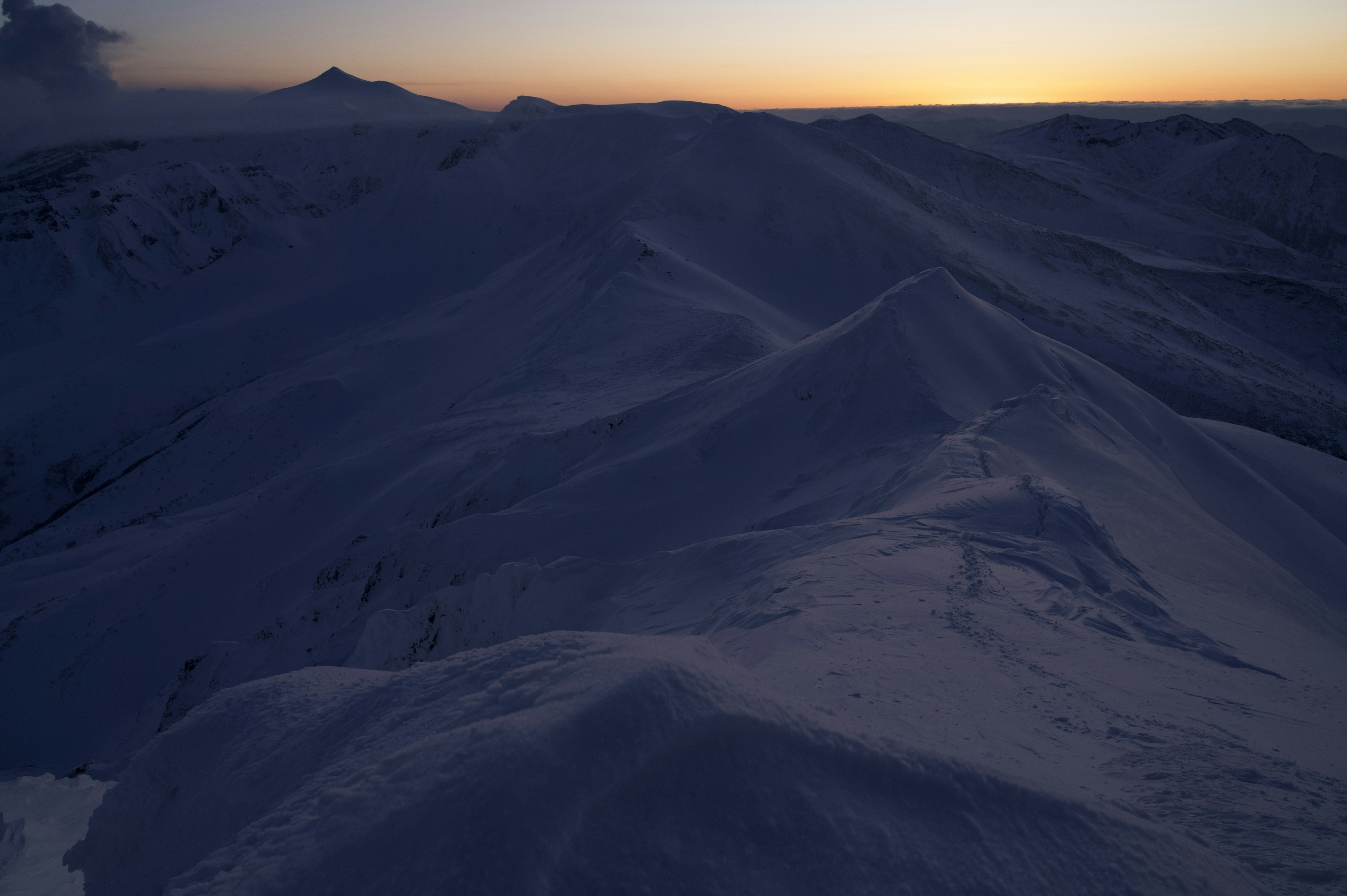 Silhouetten von schneebedeckten Bergen vor einem Sonnenuntergangshimmel