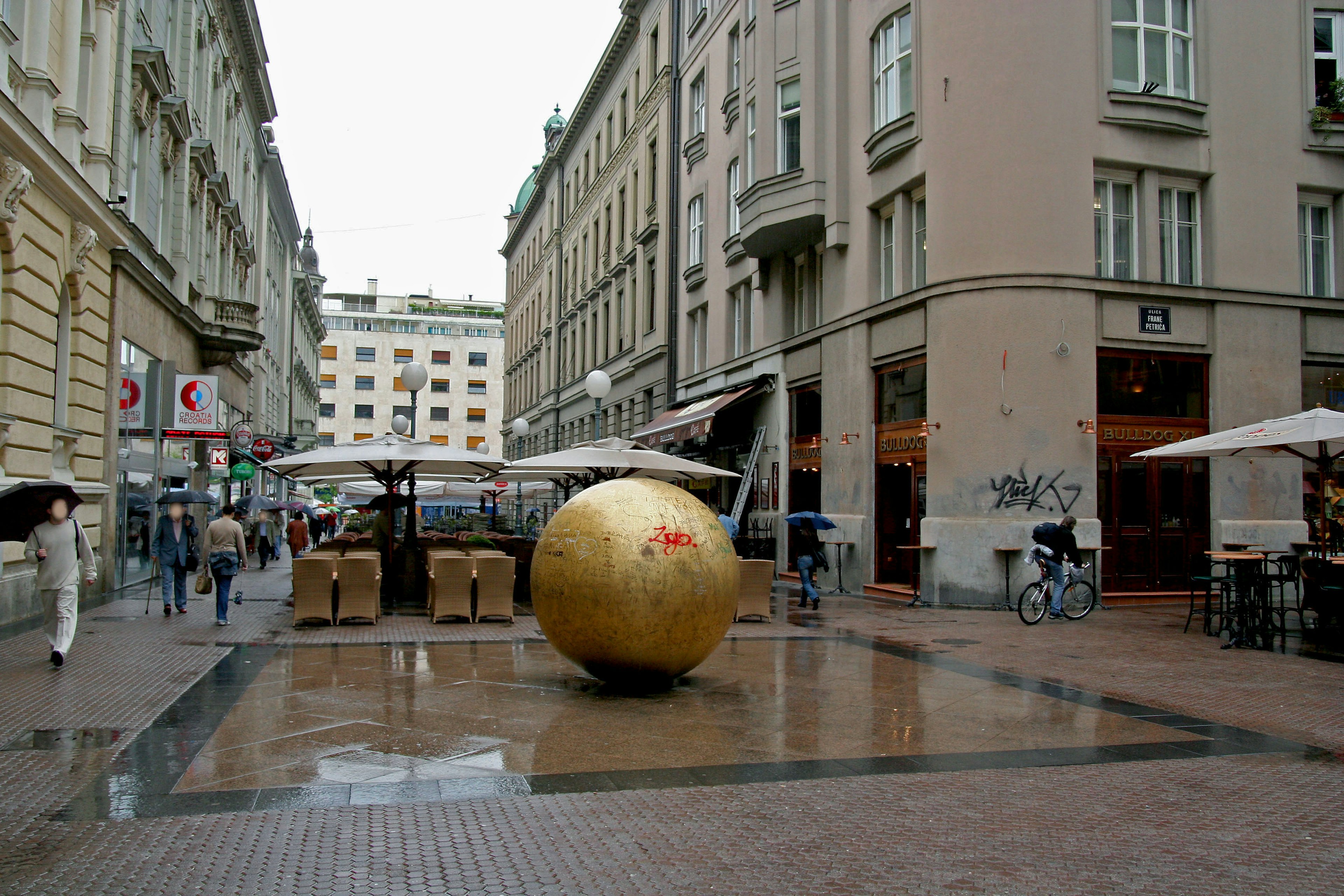 Esfera dorada en una plaza mojada por la lluvia con edificios alrededor