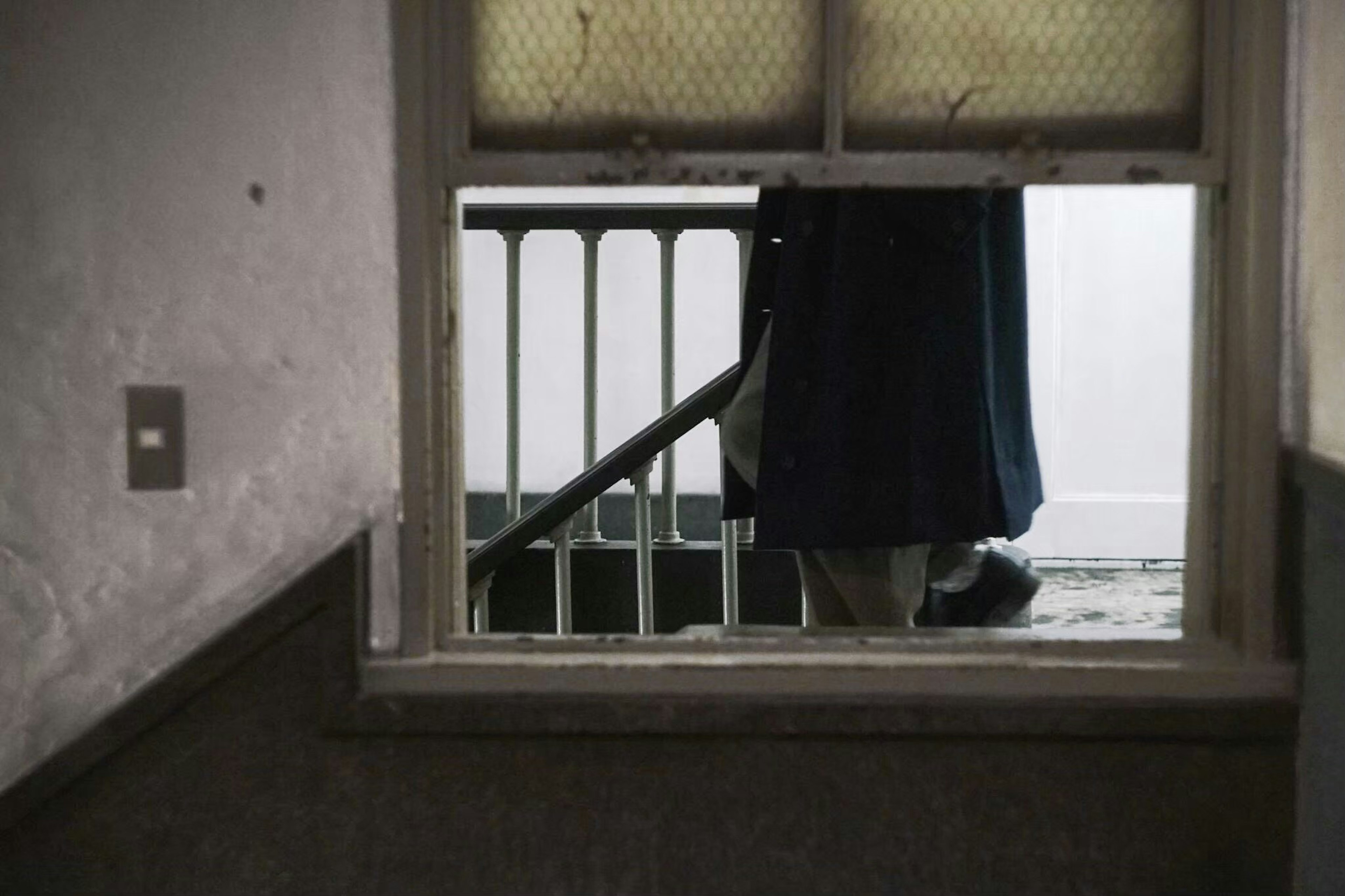 Image of a hallway with a staircase and a shadow of clothing visible through a window