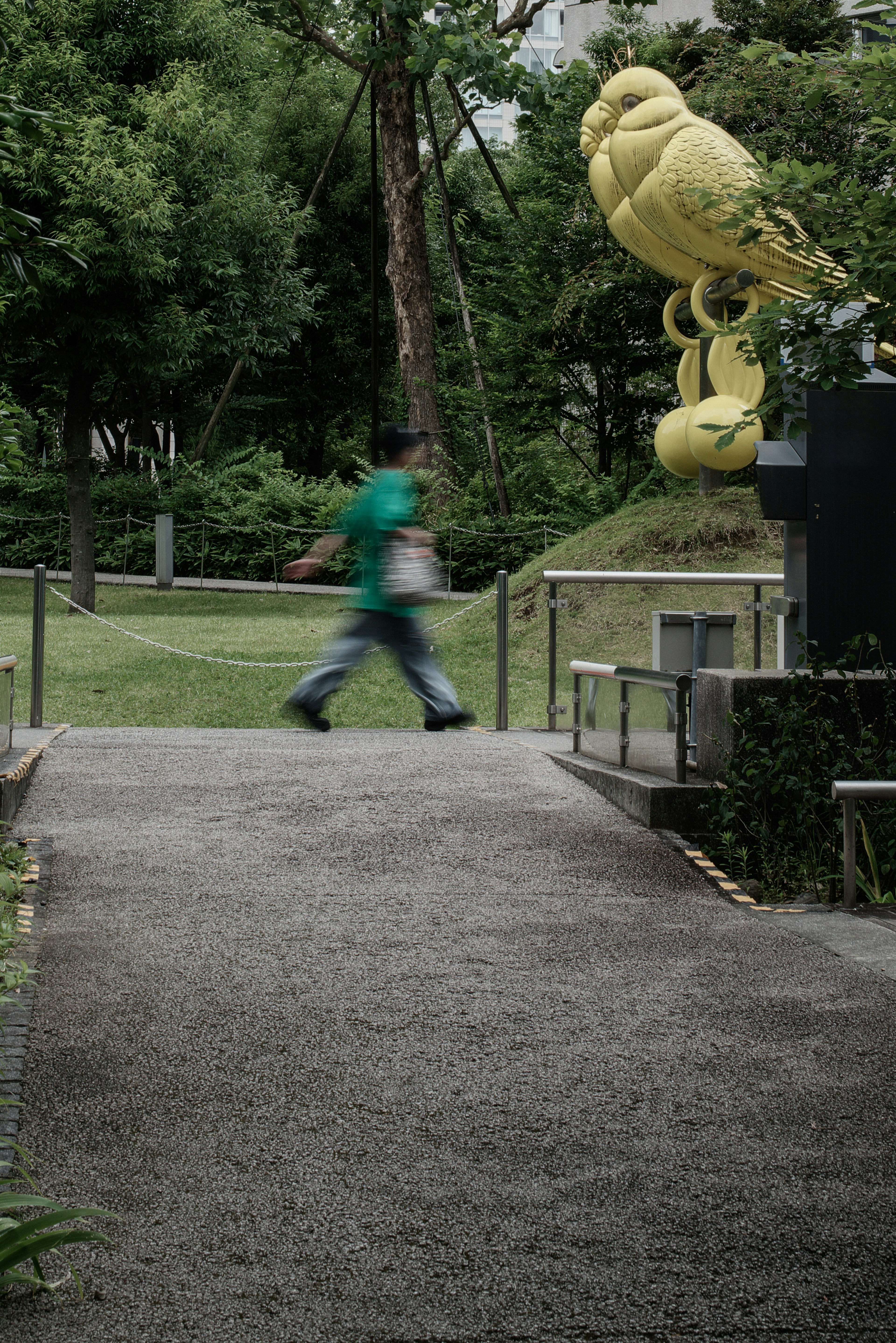 Une personne marchant le long d'un chemin de parc avec une grande sculpture d'oiseau jaune