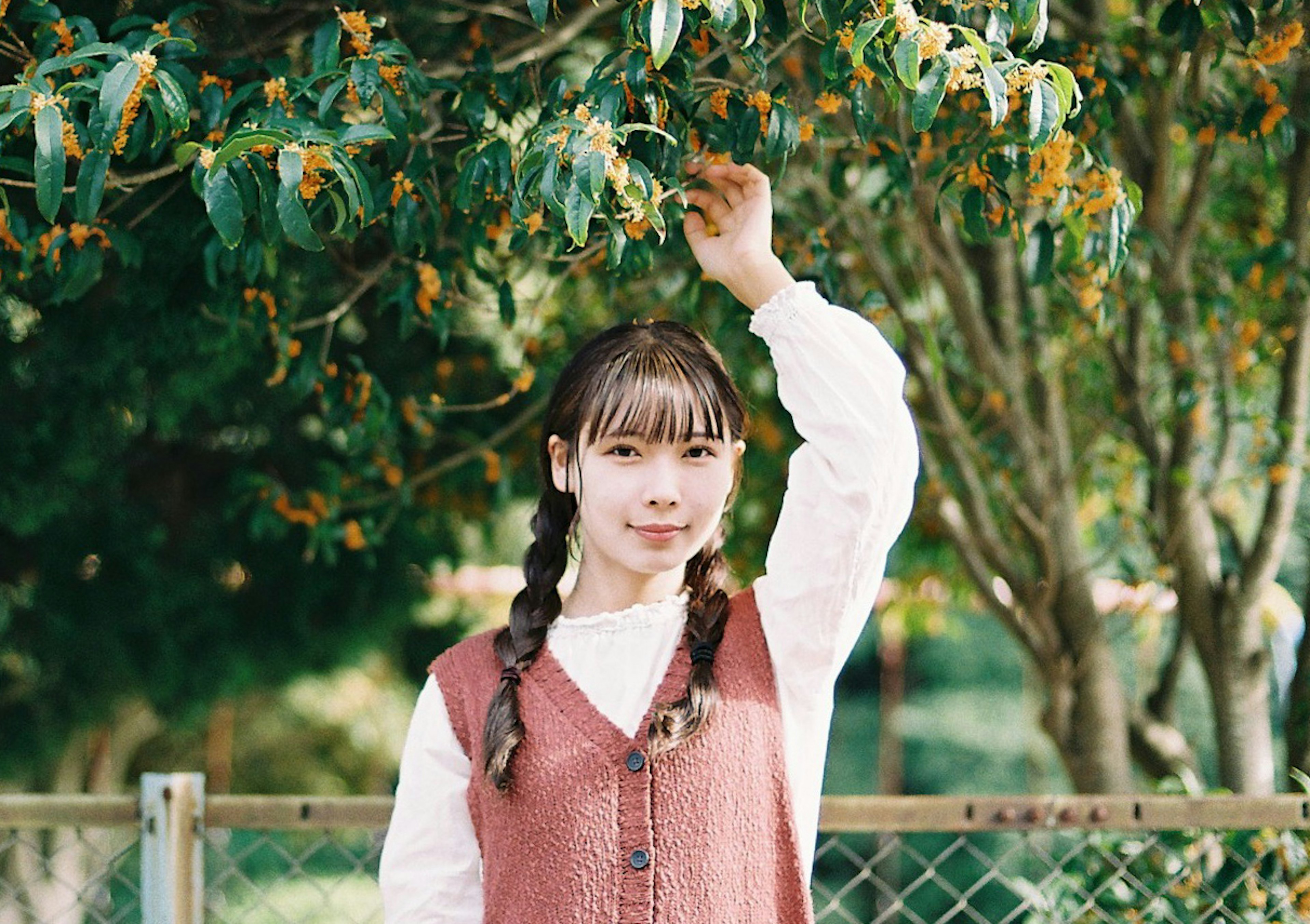 A girl smiling under a green tree with braided hair