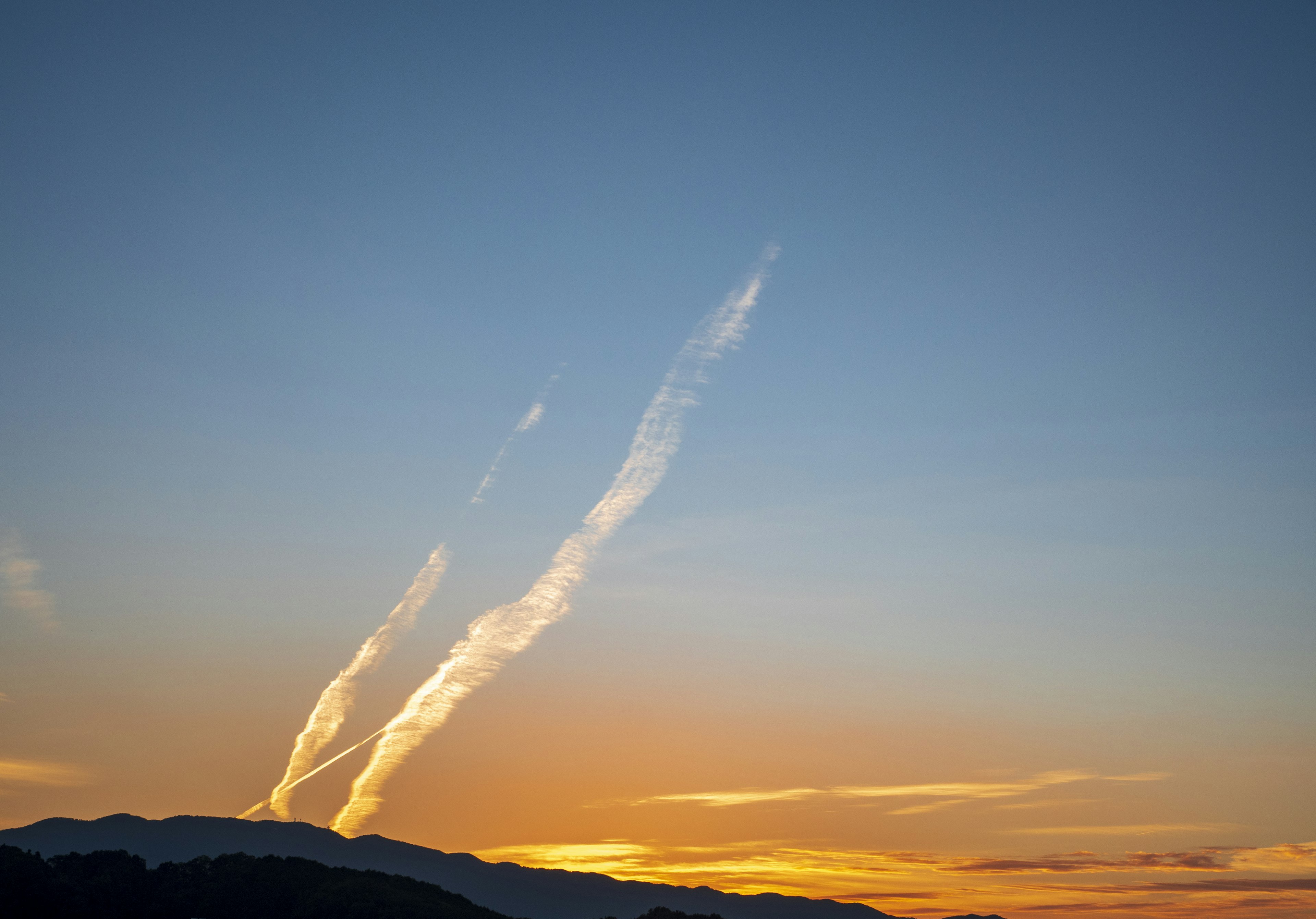 Traînées de nuages dans un ciel au coucher du soleil avec des silhouettes de montagnes