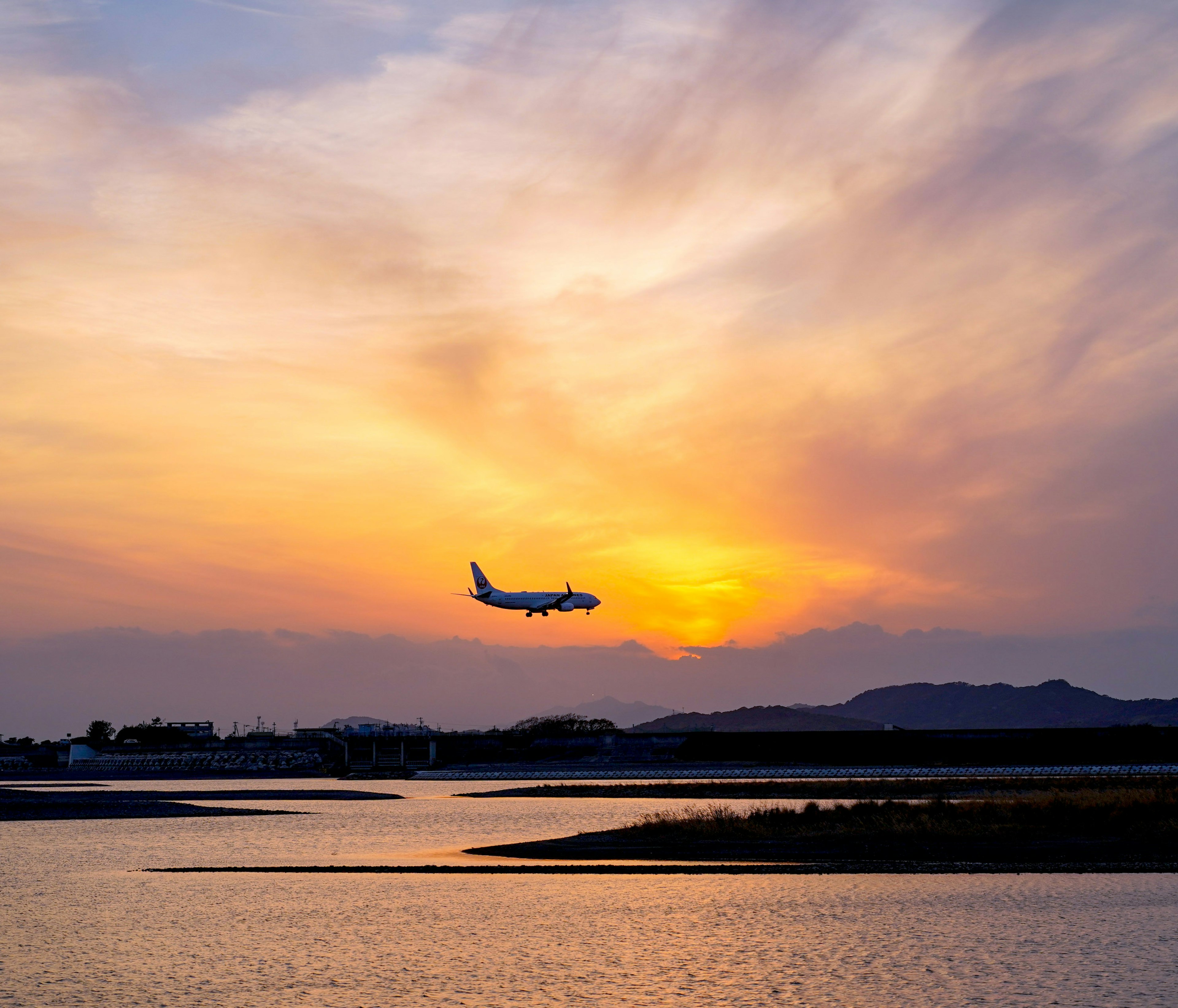 夕日の下を飛行機が飛ぶ風景 水面に映るオレンジ色の空