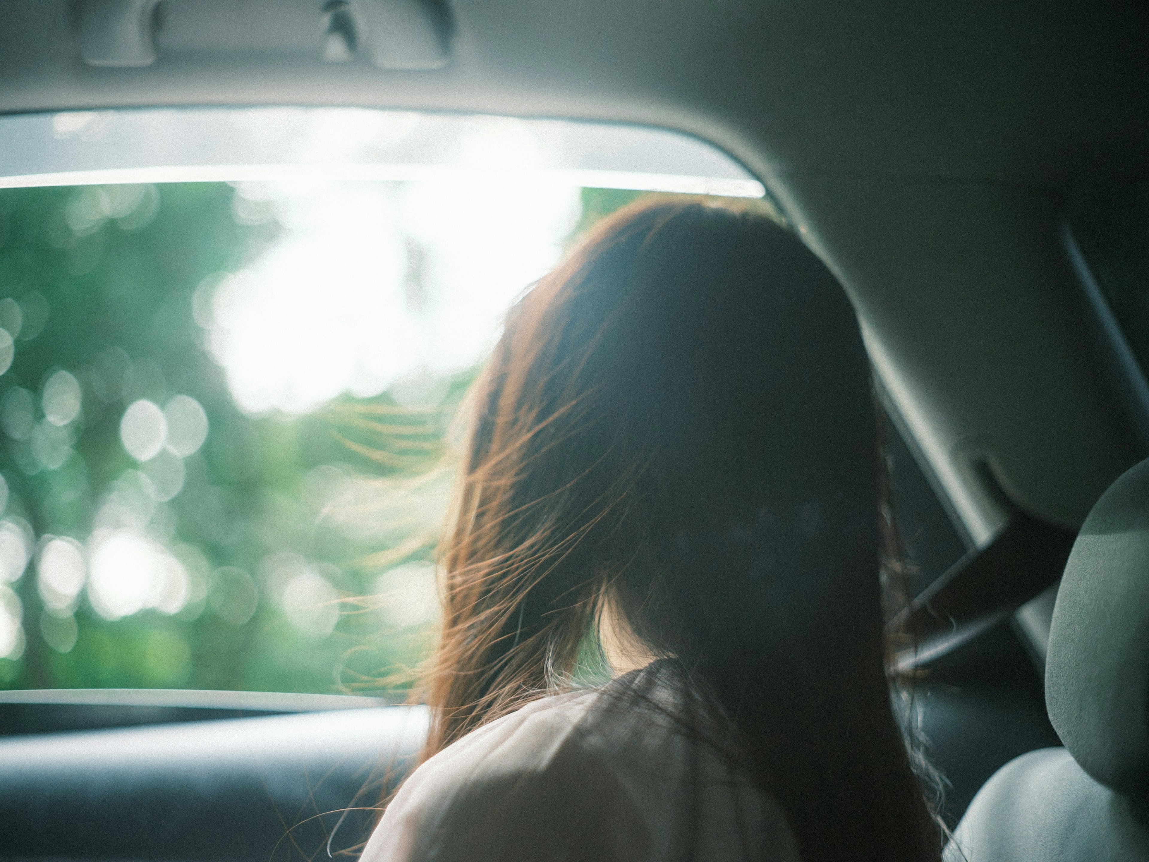 A woman looking out of a car window with hair blowing in the wind