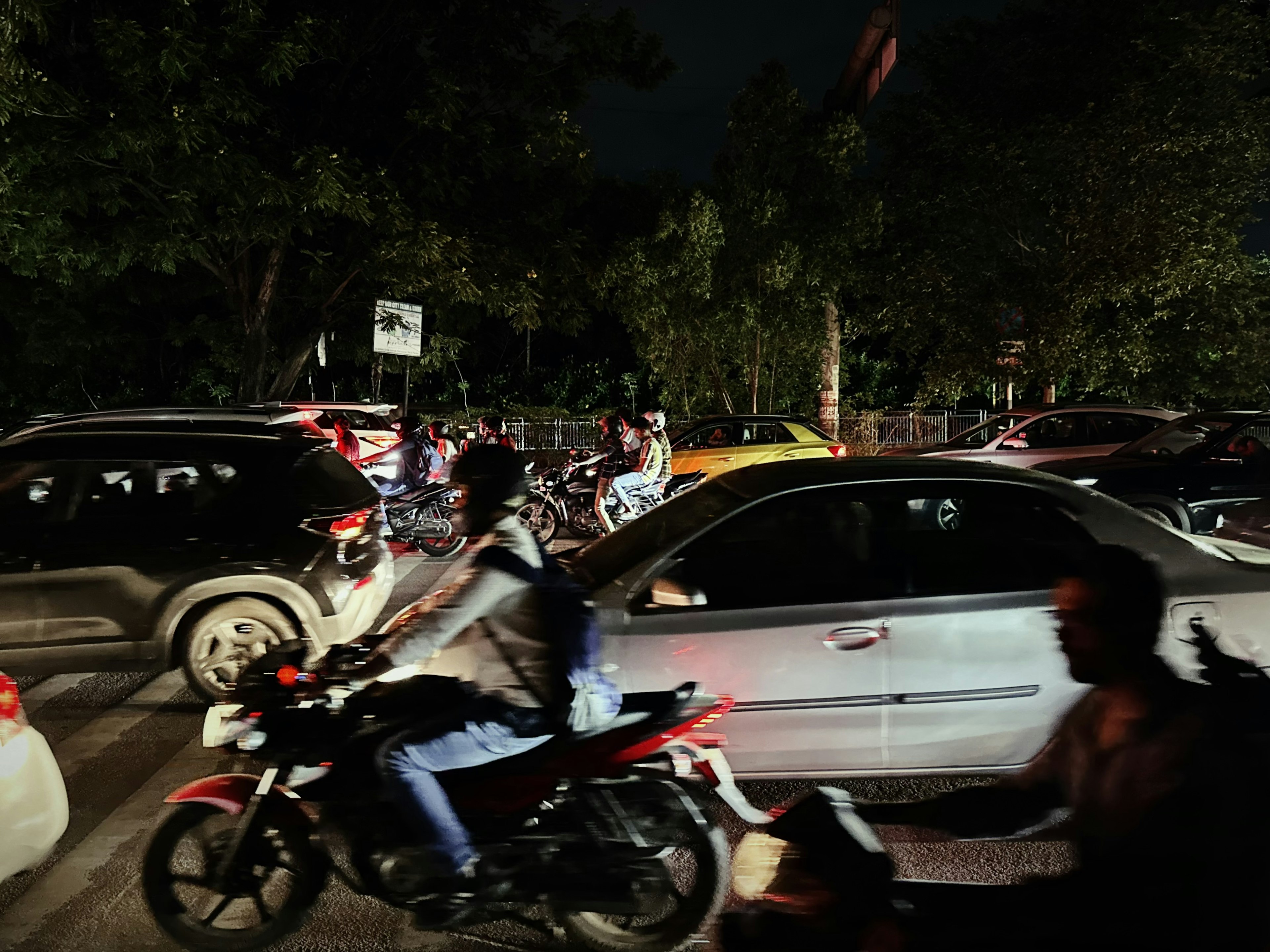 Lalu lintas malam yang sibuk dengan mobil dan sepeda motor di lingkungan yang padat