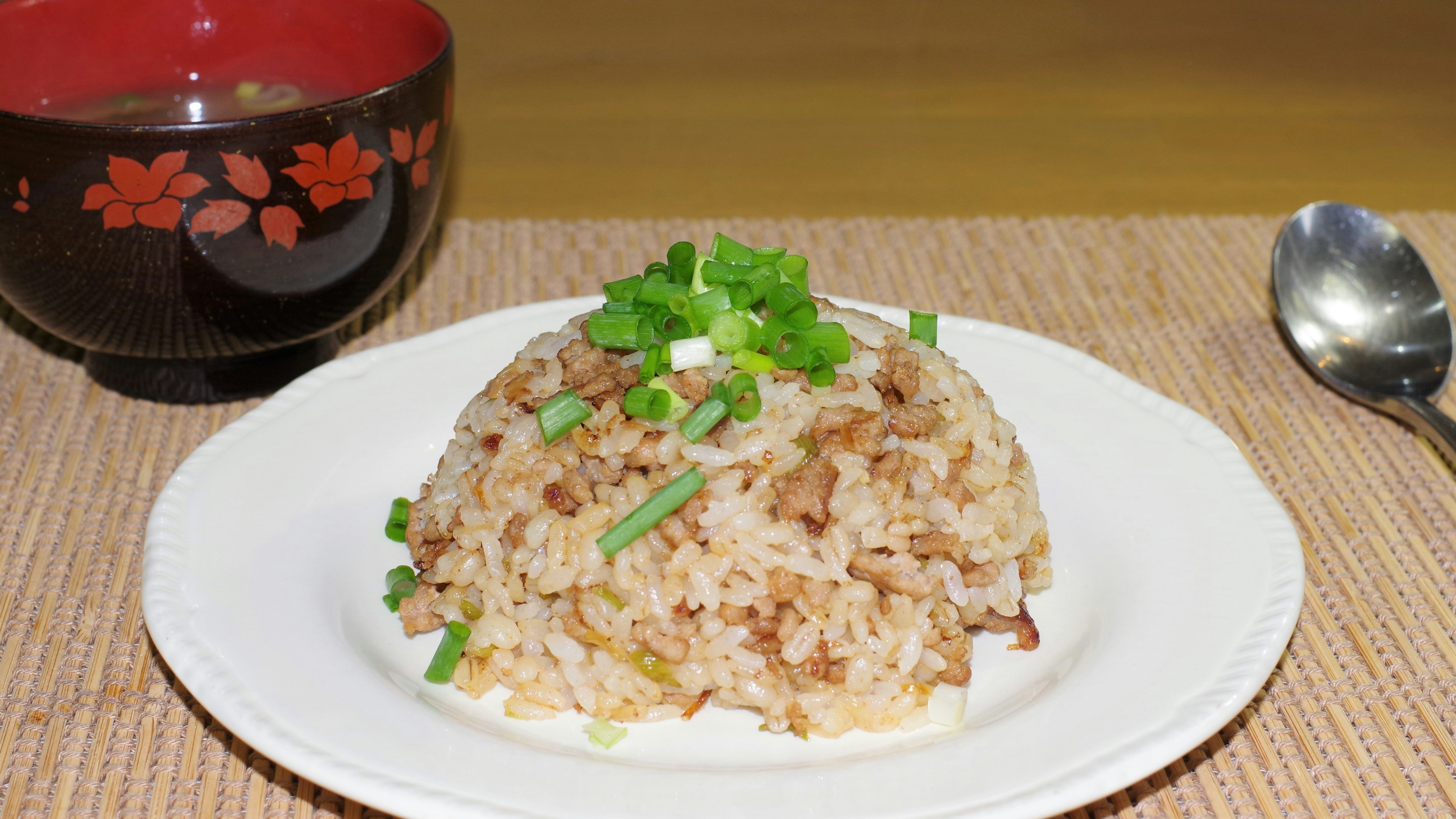 Piring nasi goreng dihiasi dengan daun bawang di samping mangkuk sup