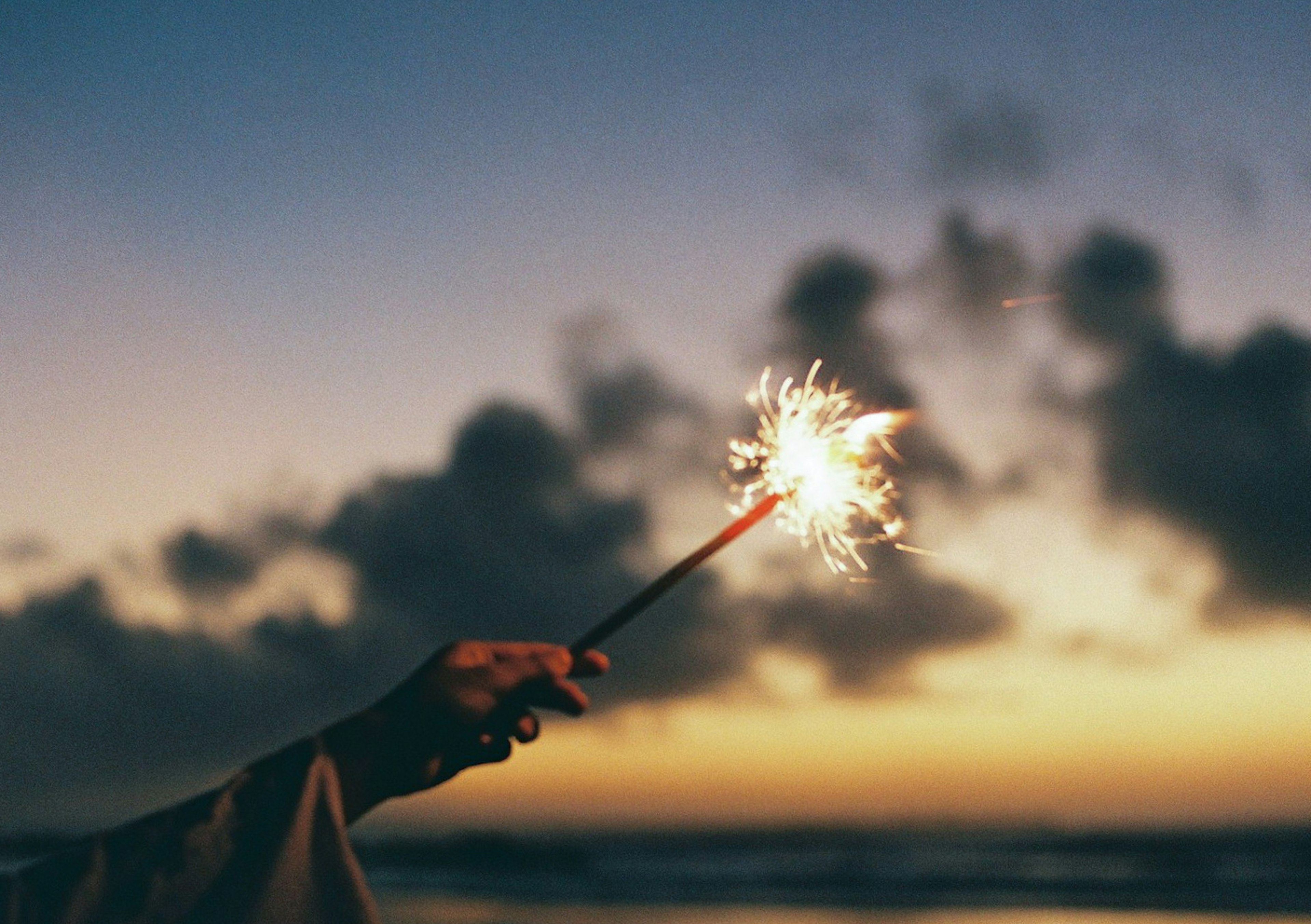 Bastoncino di fuoco d'artificio tenuto in mano al tramonto sulla spiaggia