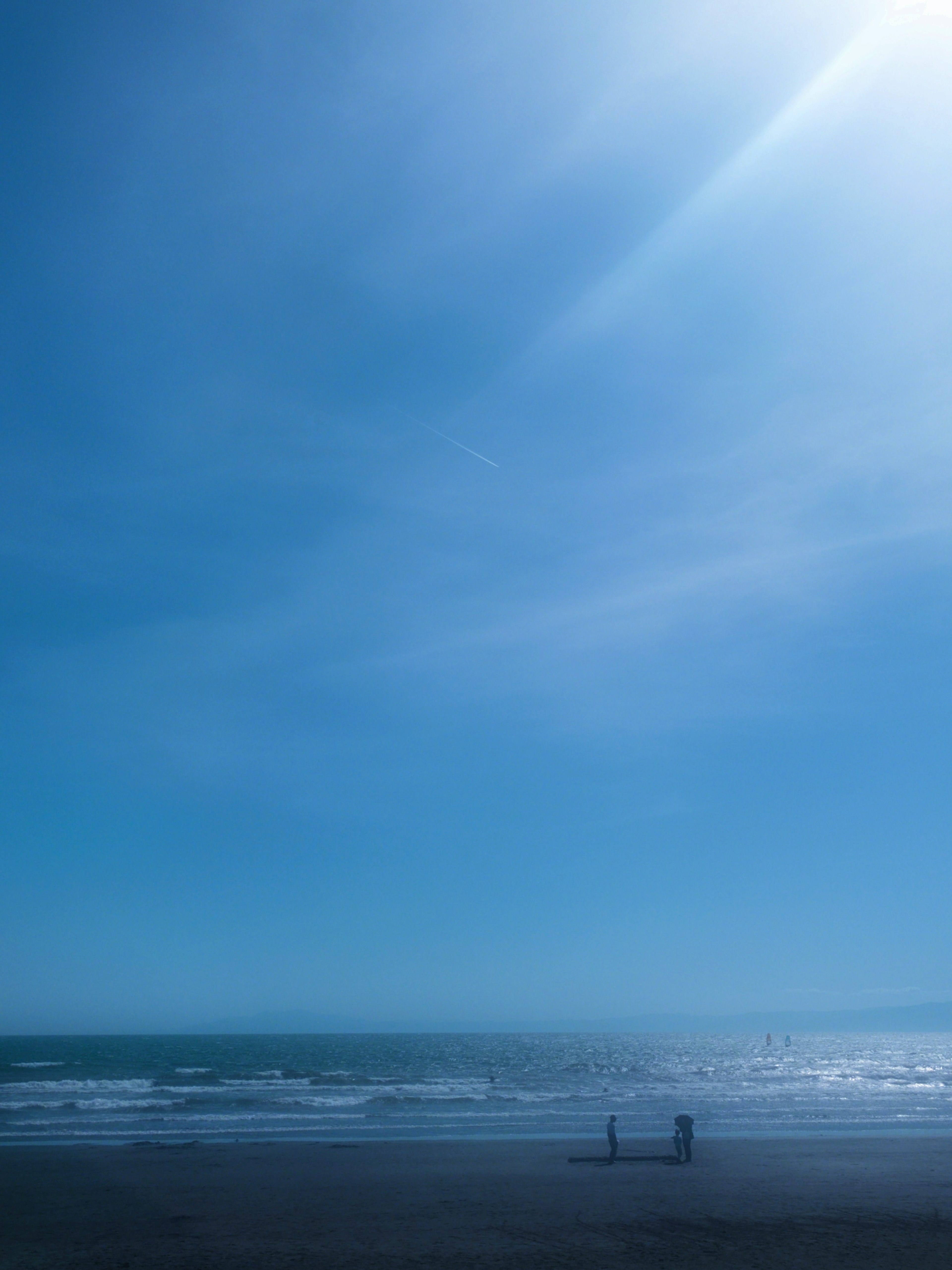 Personas de pie en una playa con cielo azul y océano