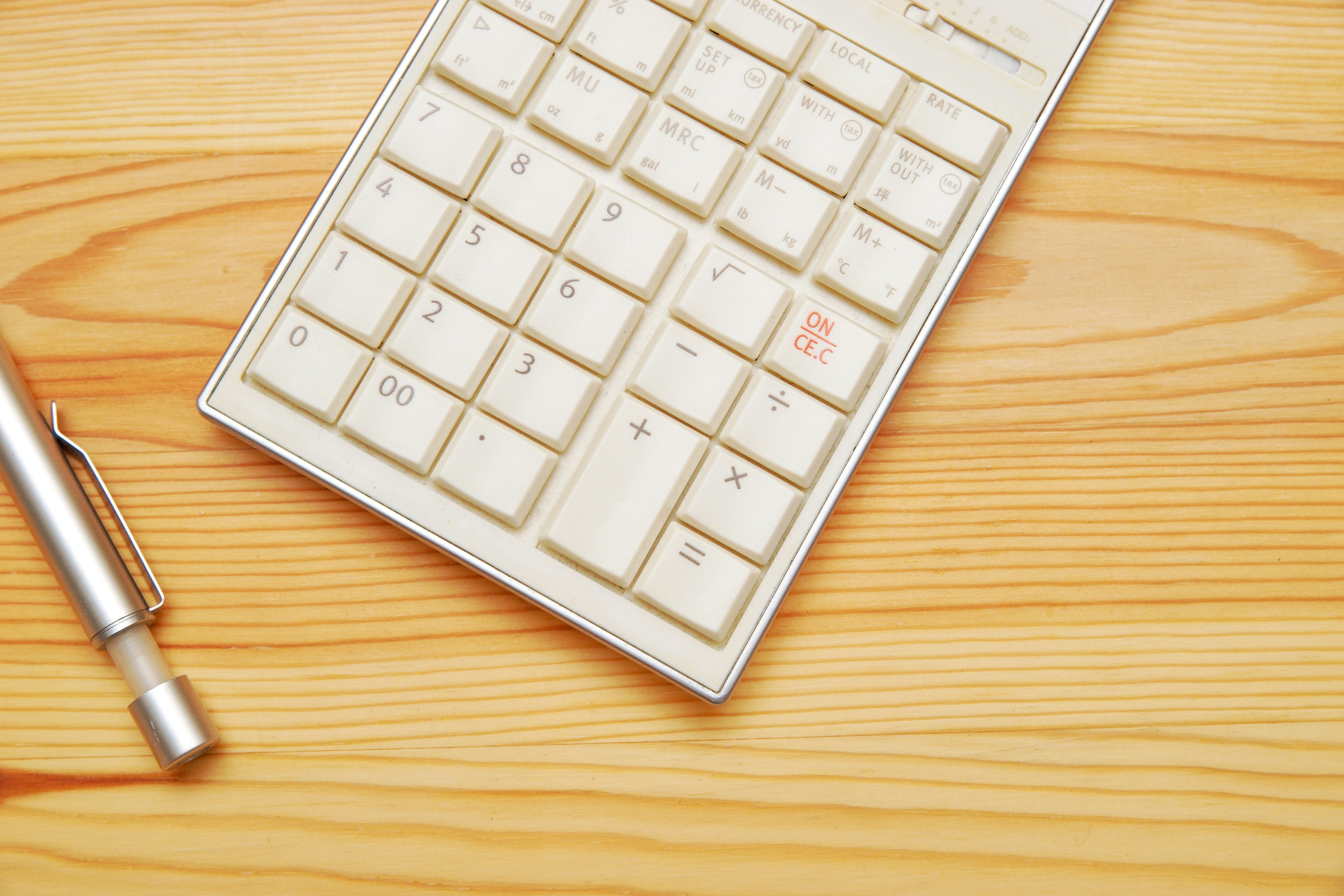 A white calculator and a pen on a wooden table