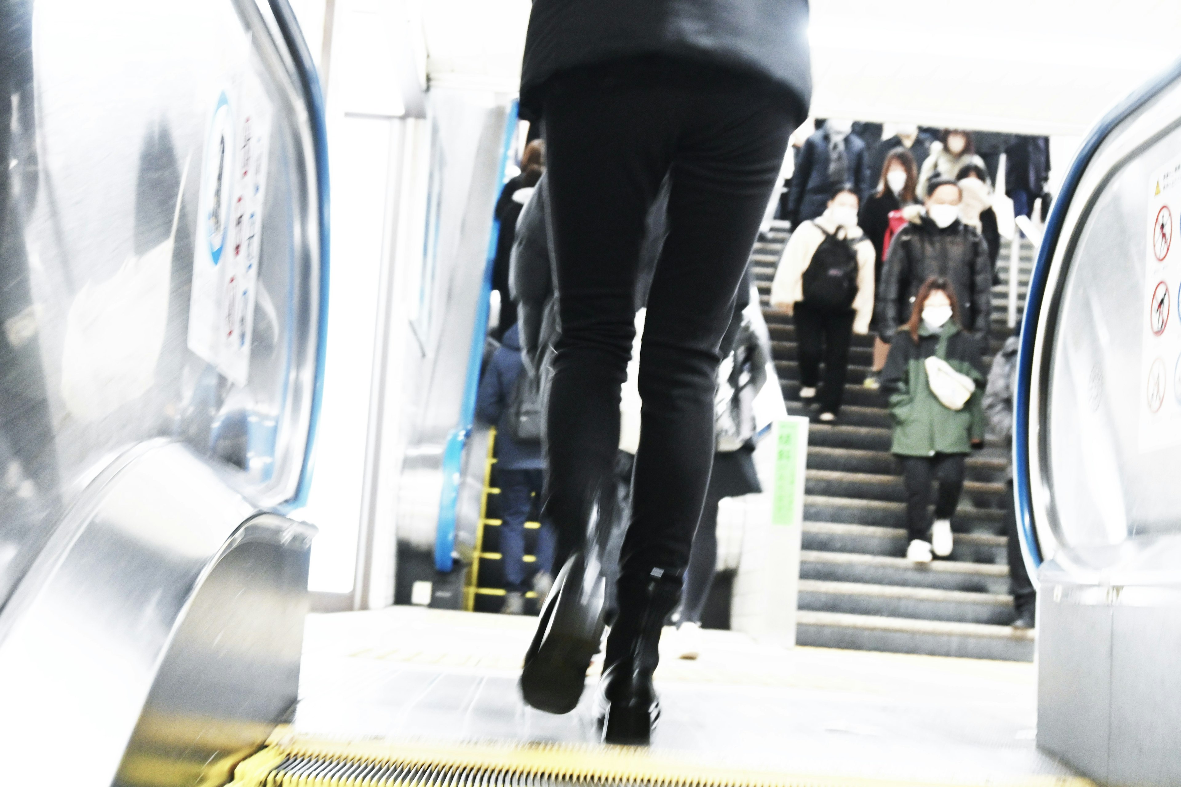 Person in schwarzen Hosen, die eine Rolltreppe hinaufgeht, mit Menschen im Hintergrund