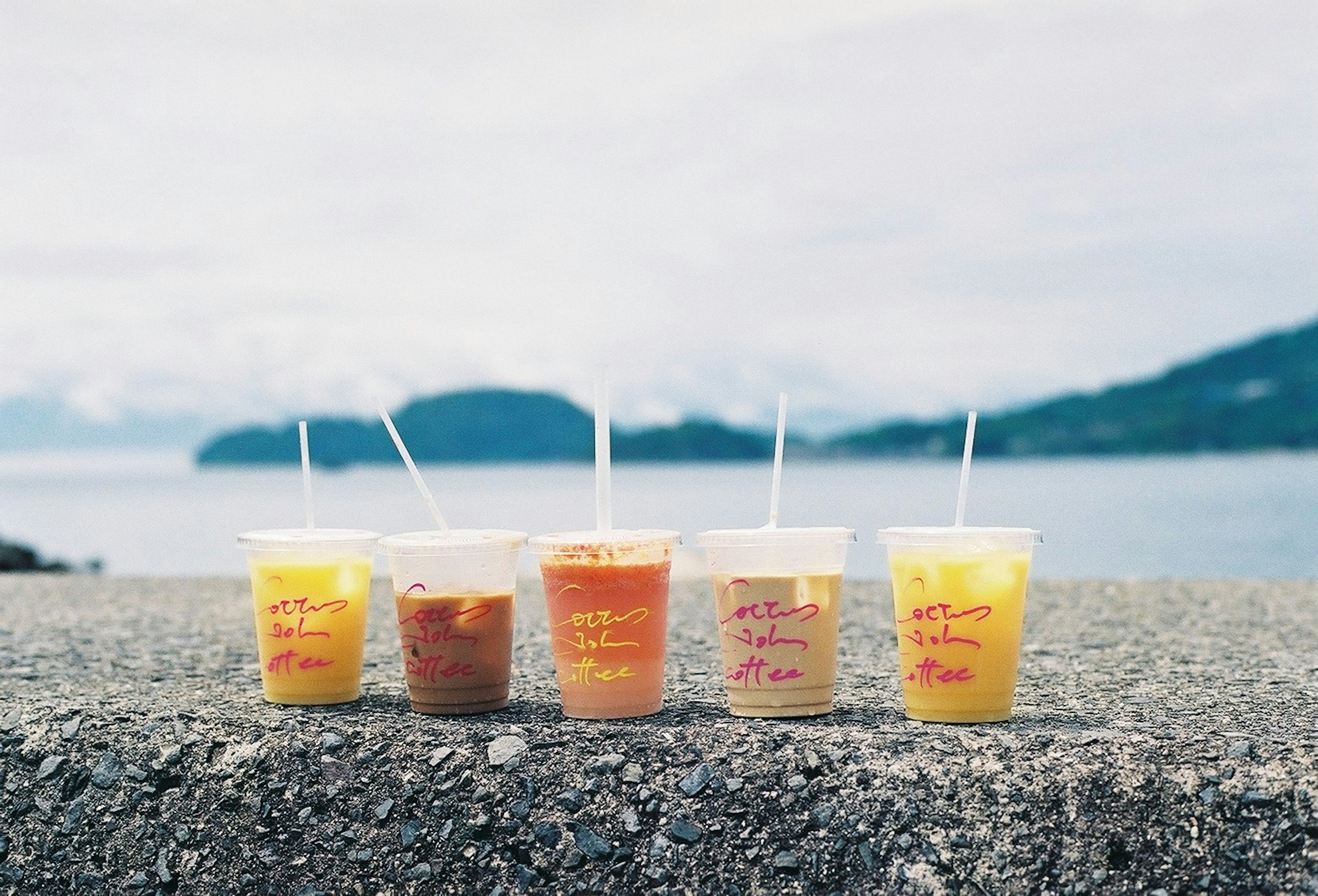 海のそばに並べられたカラフルな飲み物のカップ