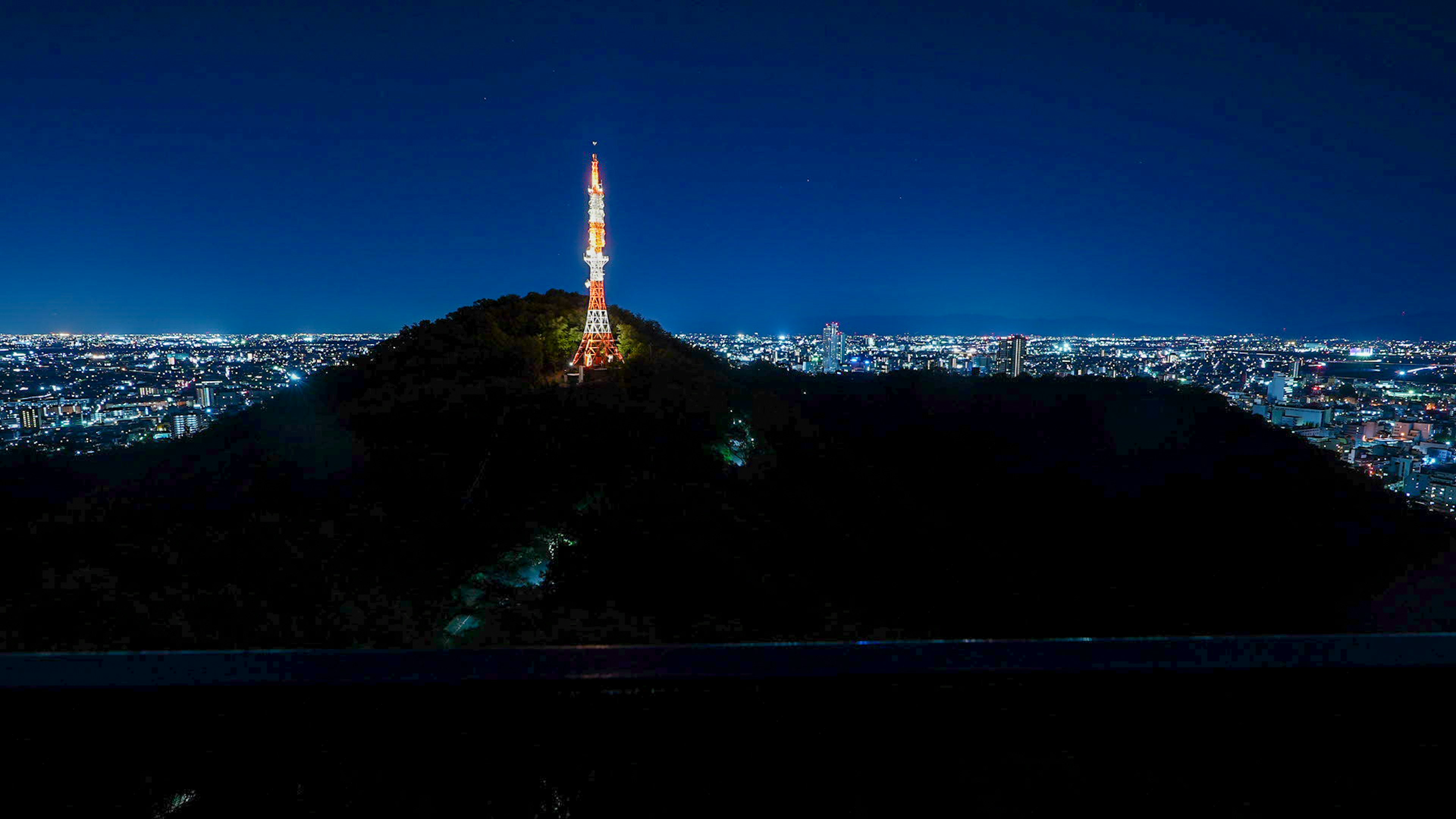 Tour illuminée la nuit surplombant une skyline urbaine