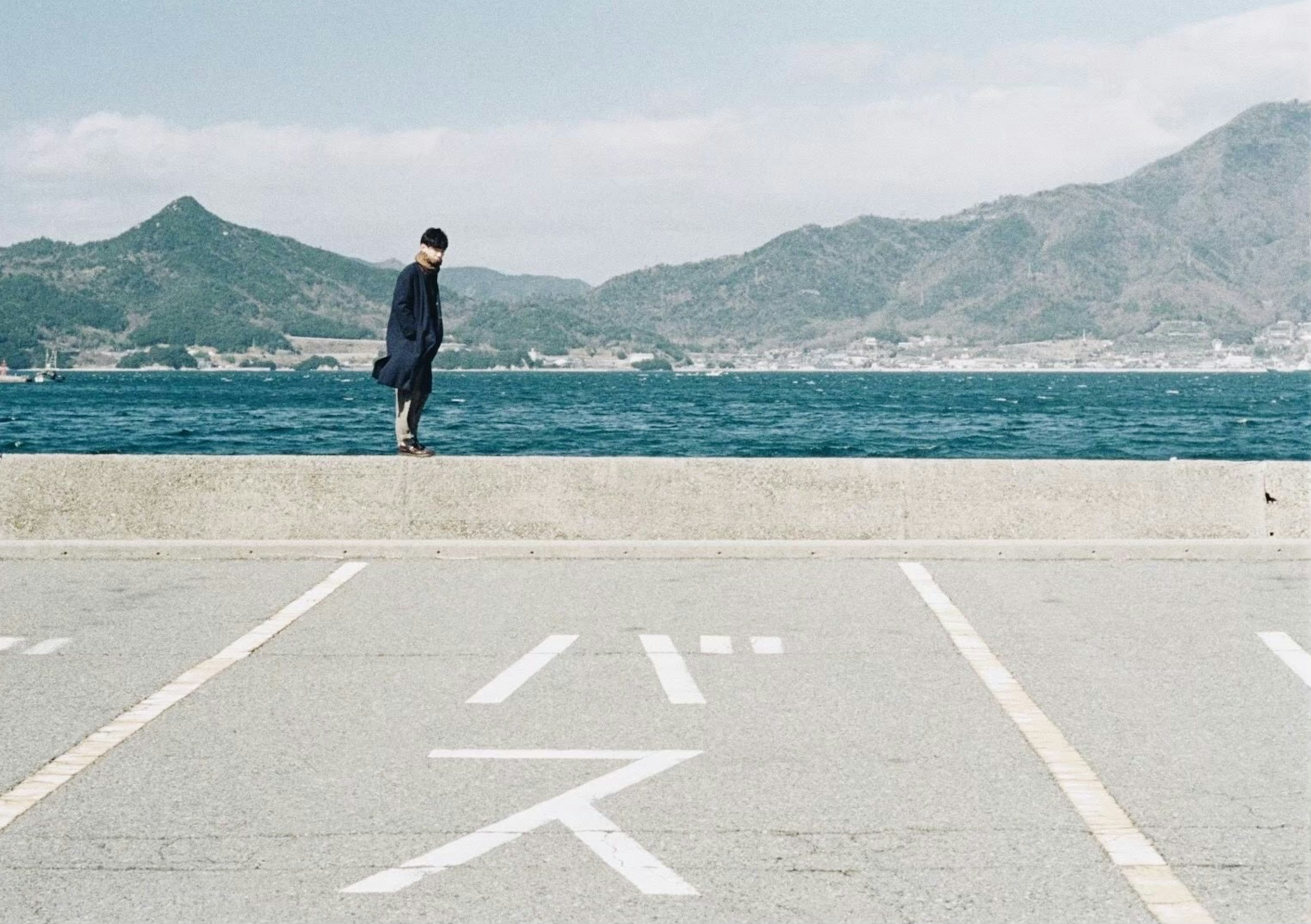 Person standing near the sea with mountains in the background