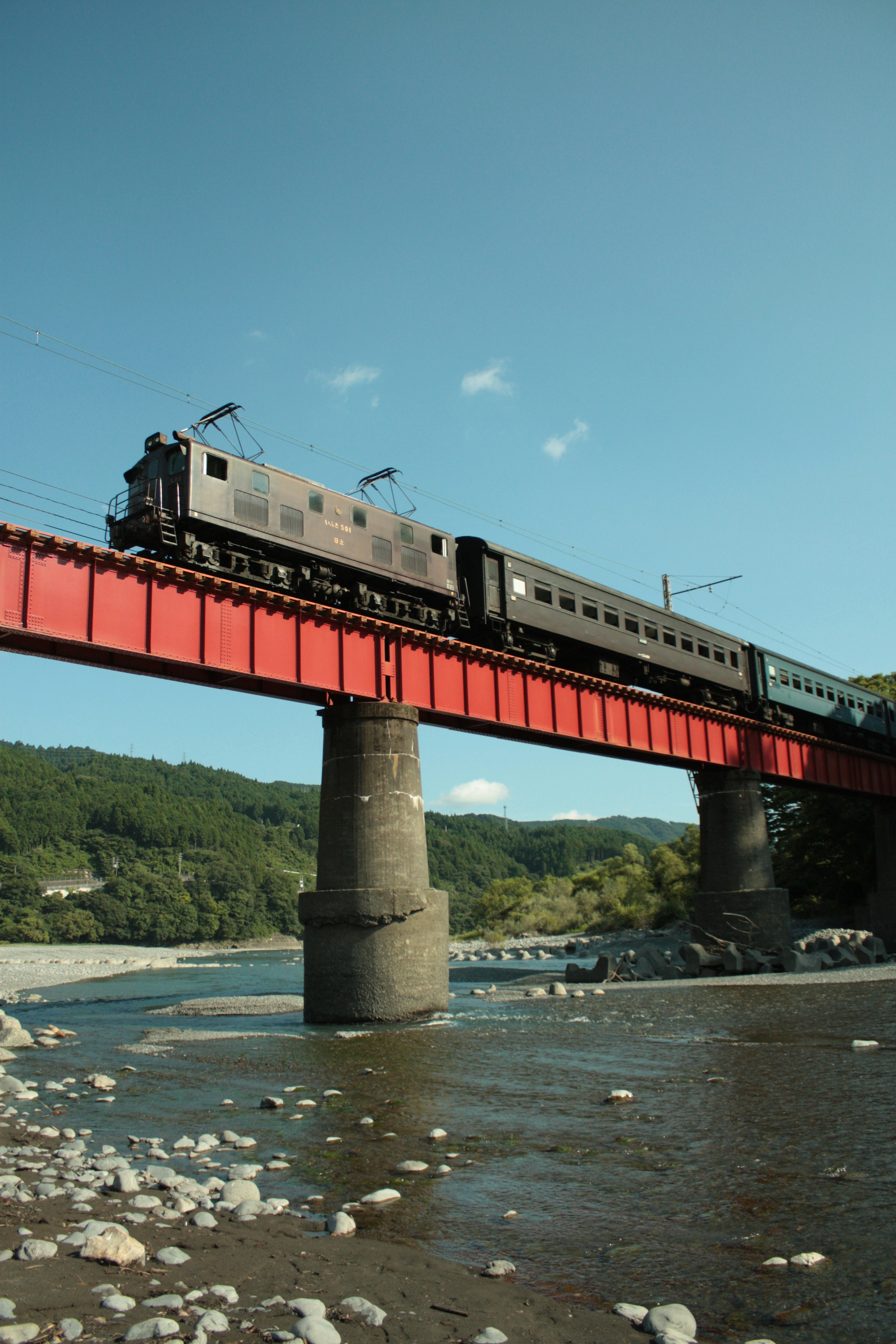 Schwarzer Zug überquert eine rote Brücke über einen Fluss